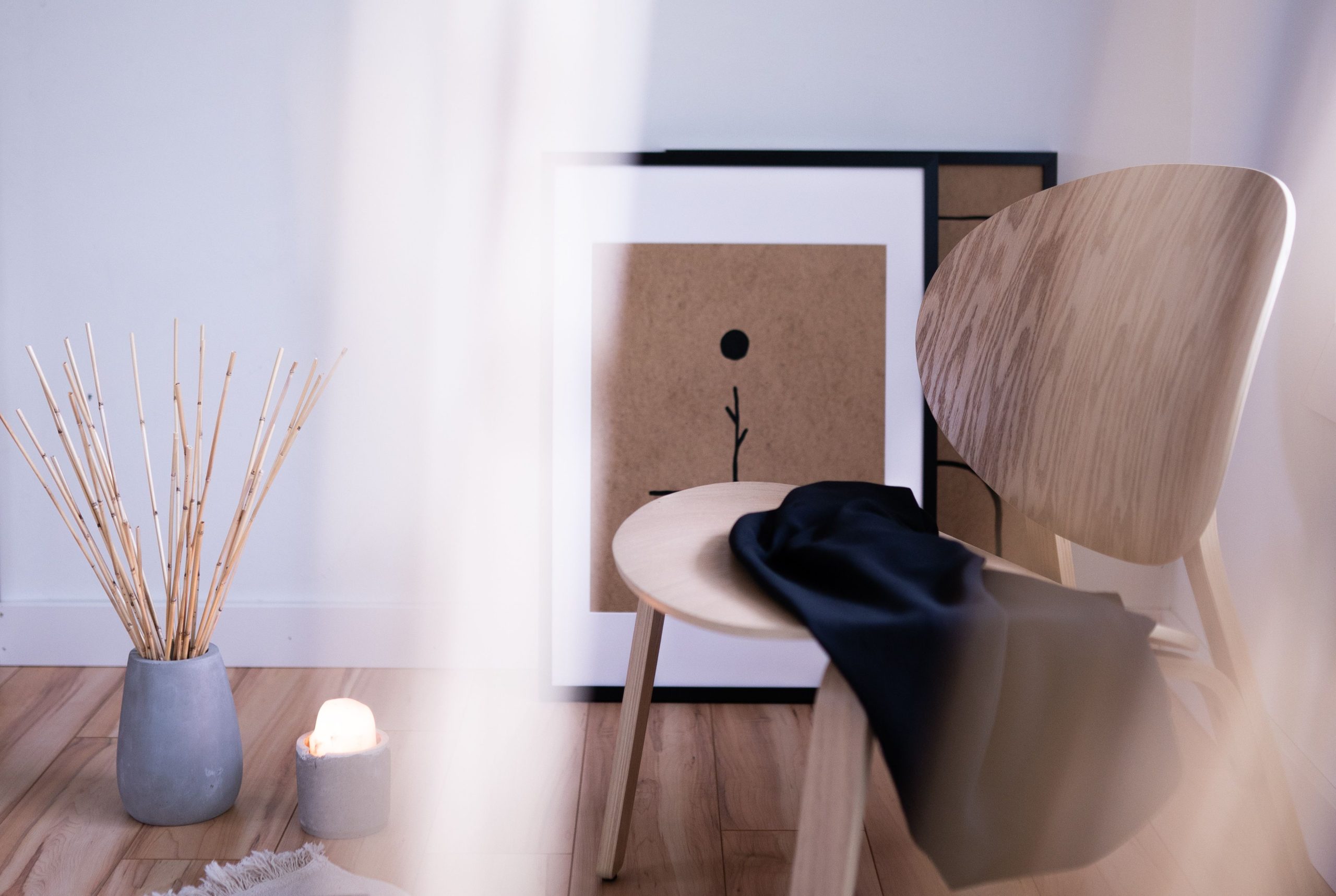Elegant minimalist interior featuring a wooden chair, bamboo sticks, and artistic picture frames.