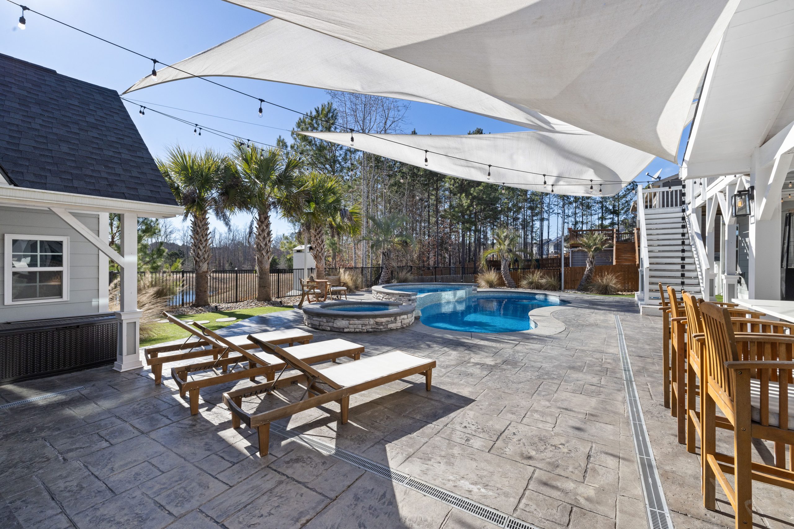 Elegant outdoor pool area featuring lounge chairs, palm trees, and sun sails under a clear blue sky.