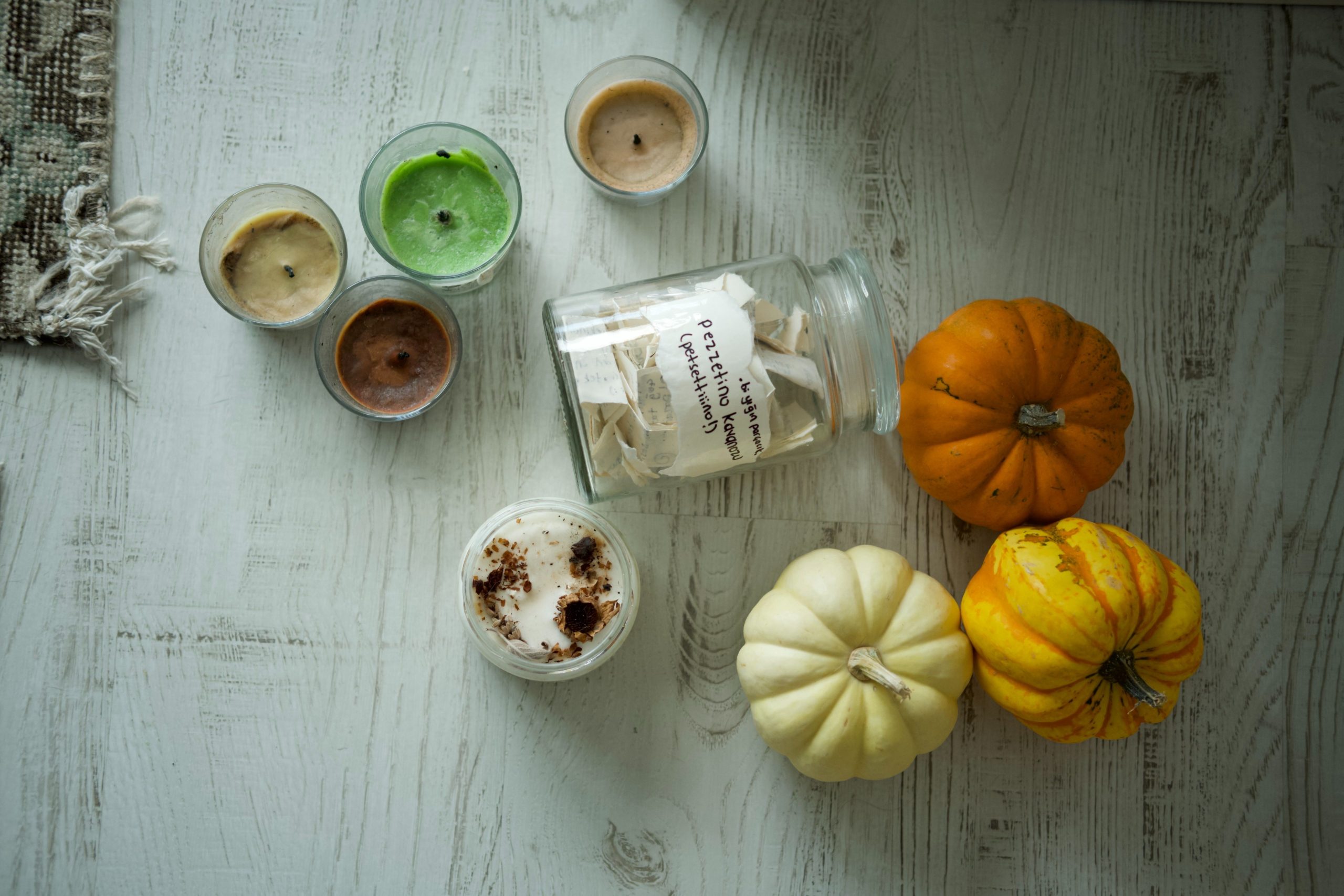 Flat lay of cozy autumn decor with colorful pumpkins and scented candles on a rustic wooden table.