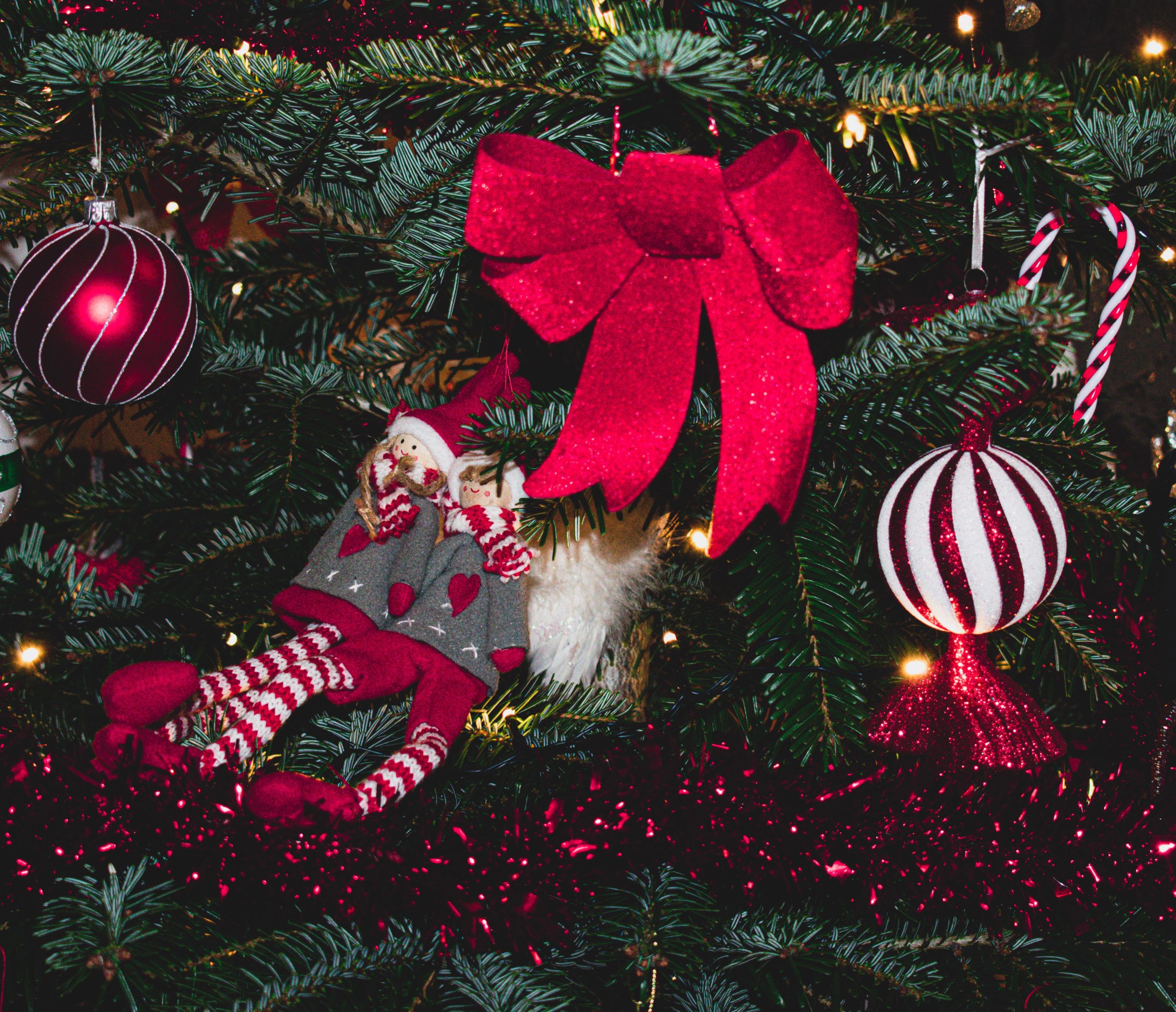Holiday-themed Christmas tree with colorful ornaments and decorative lights, featuring a vibrant red bow and playful elf dolls.