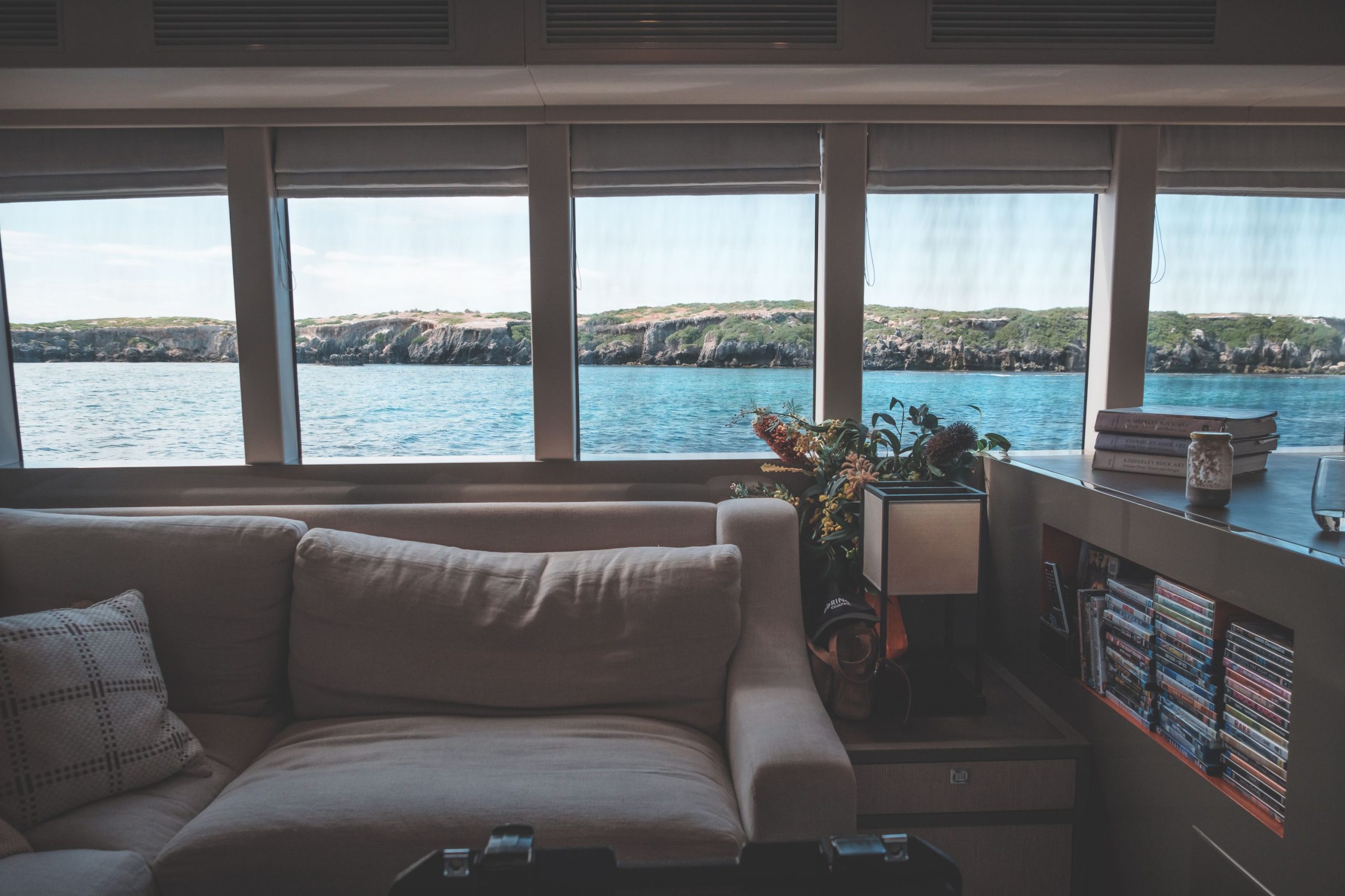 Interior of living room inside of modern yacht with comfortable sofa and windows overlooking blue sea and rocky islands during cruise in sunlight