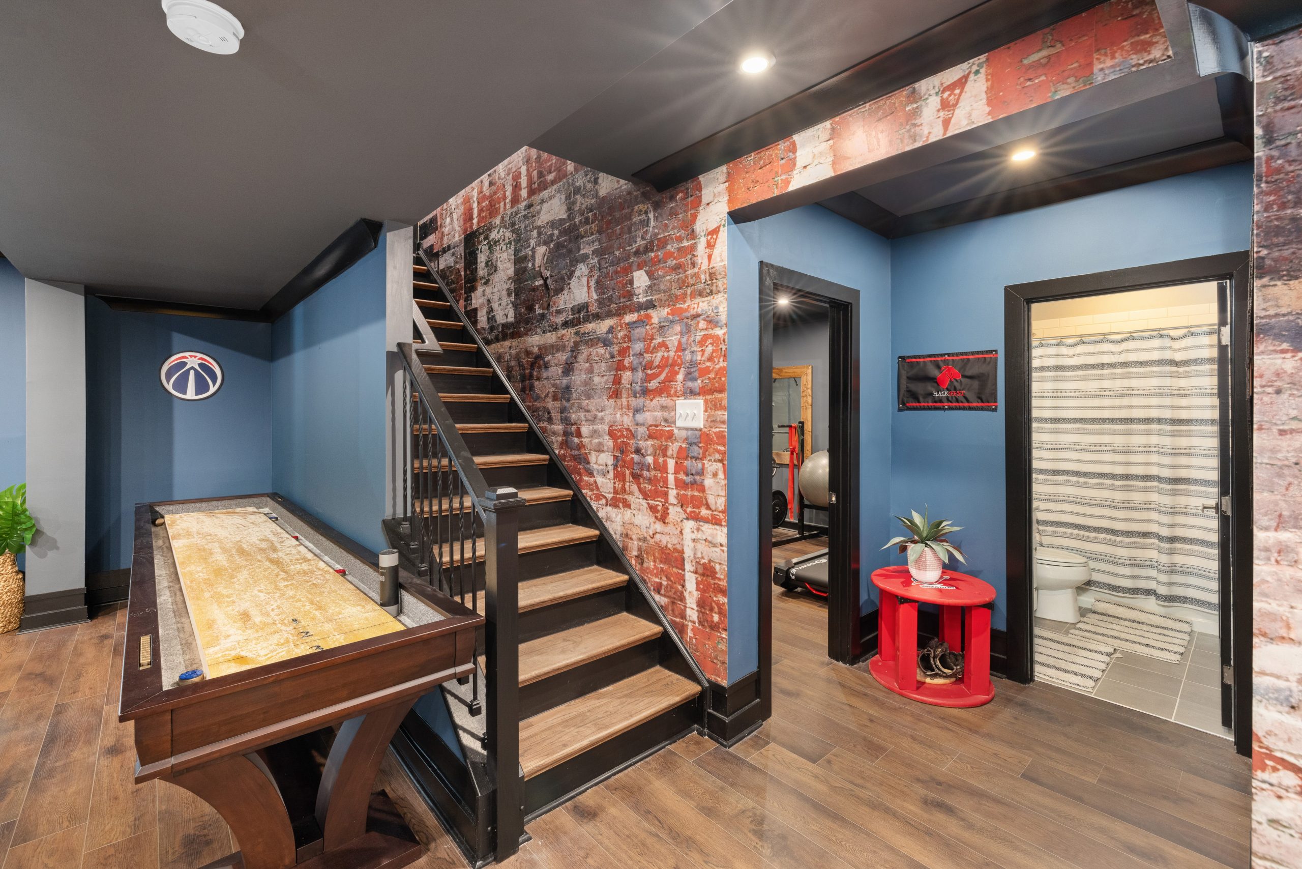 Modern basement interior with game table, rustic brick walls, and a stairway.