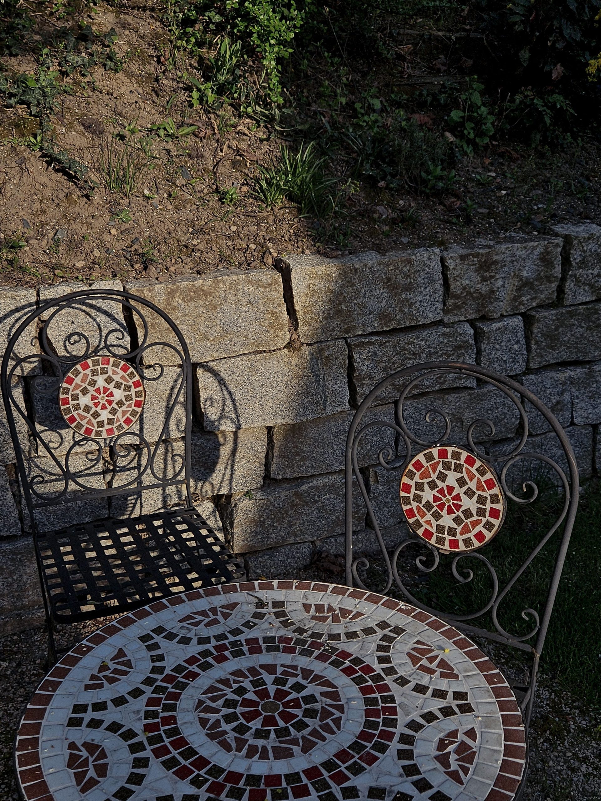 Ornate mosaic table and chairs in a sunny outdoor stone patio.