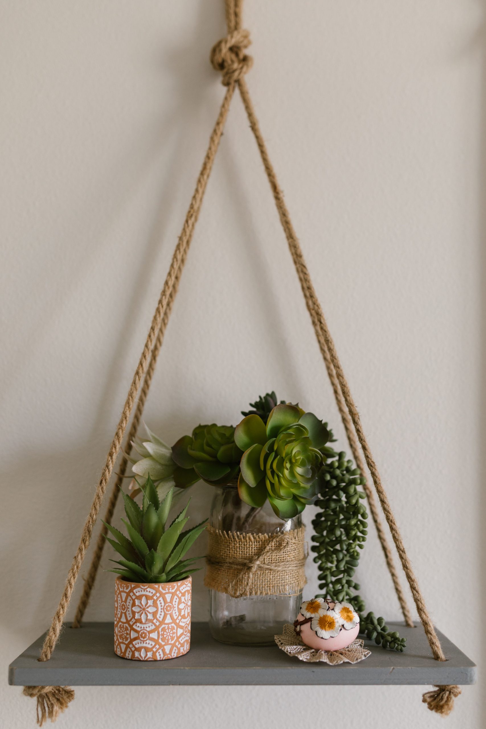 Stylish hanging rope shelf featuring succulent plants and decorative items.
