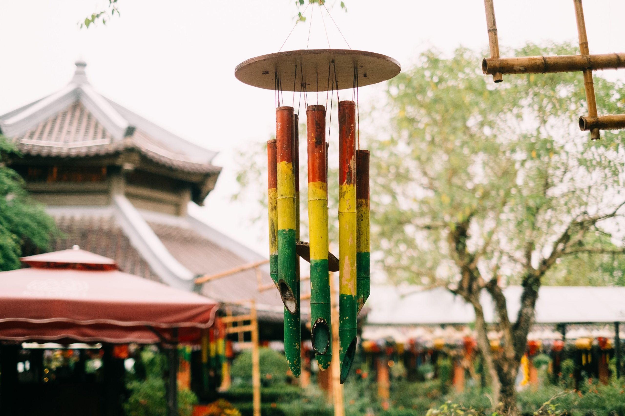 Vibrant bamboo wind chimes hanging in a tranquil Asian garden setting with a traditional building backdrop.