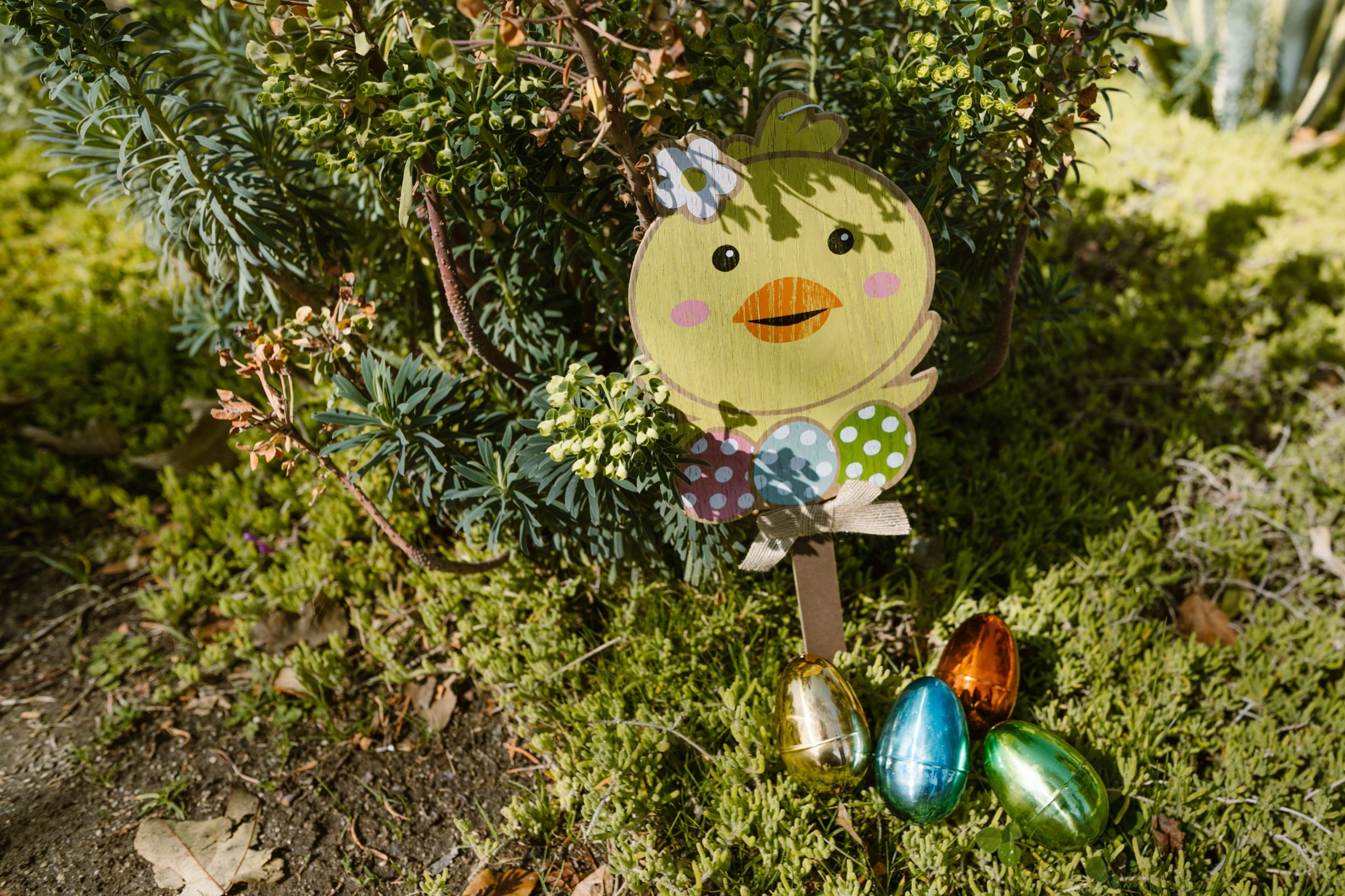 Vibrant Easter decorations with eggs and chick in a lush garden setting.