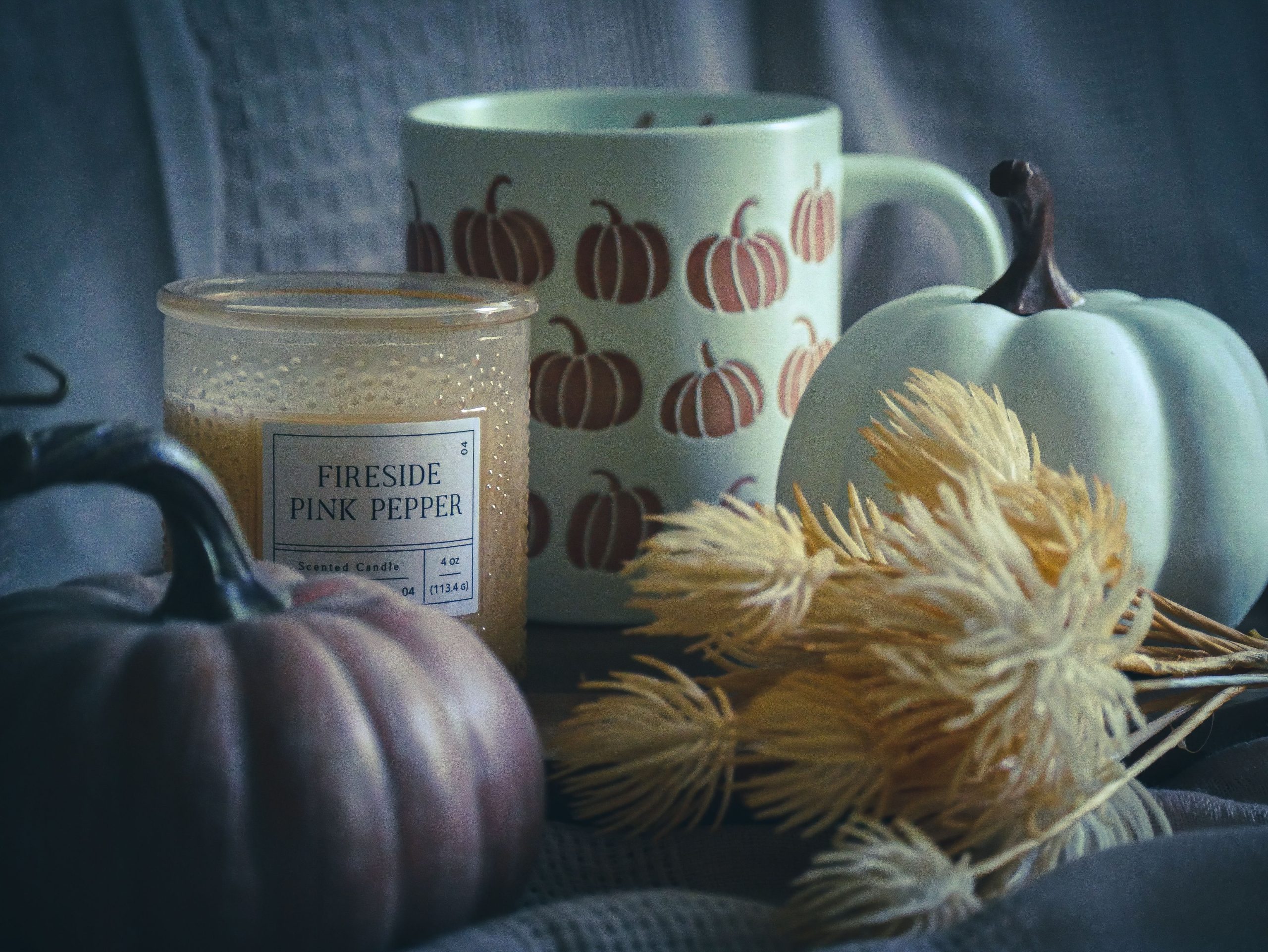 Warm autumn setup featuring a fireside pink pepper candle and pumpkin mug for cozy vibes.