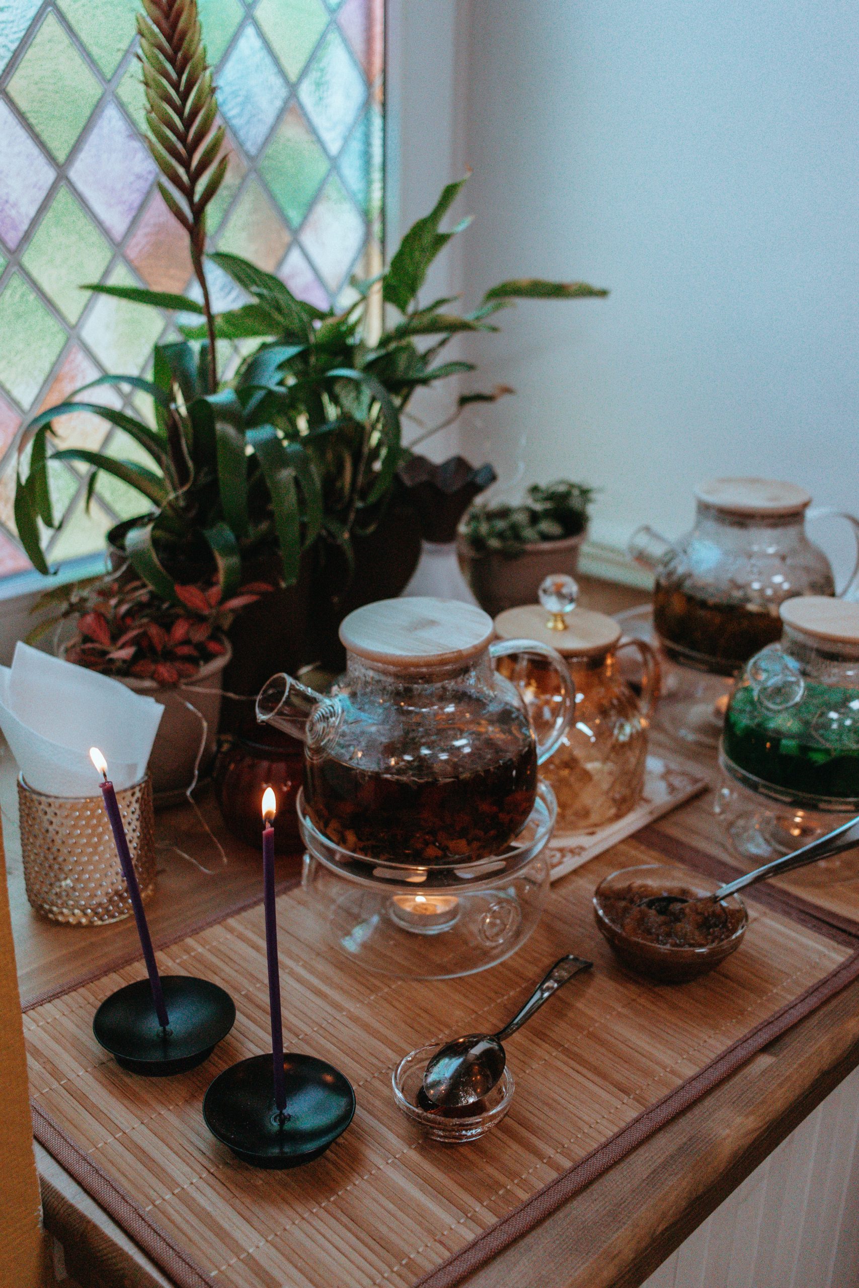 Warm indoor scene with brewed herbal teapots, plants, and candles on a wooden table.