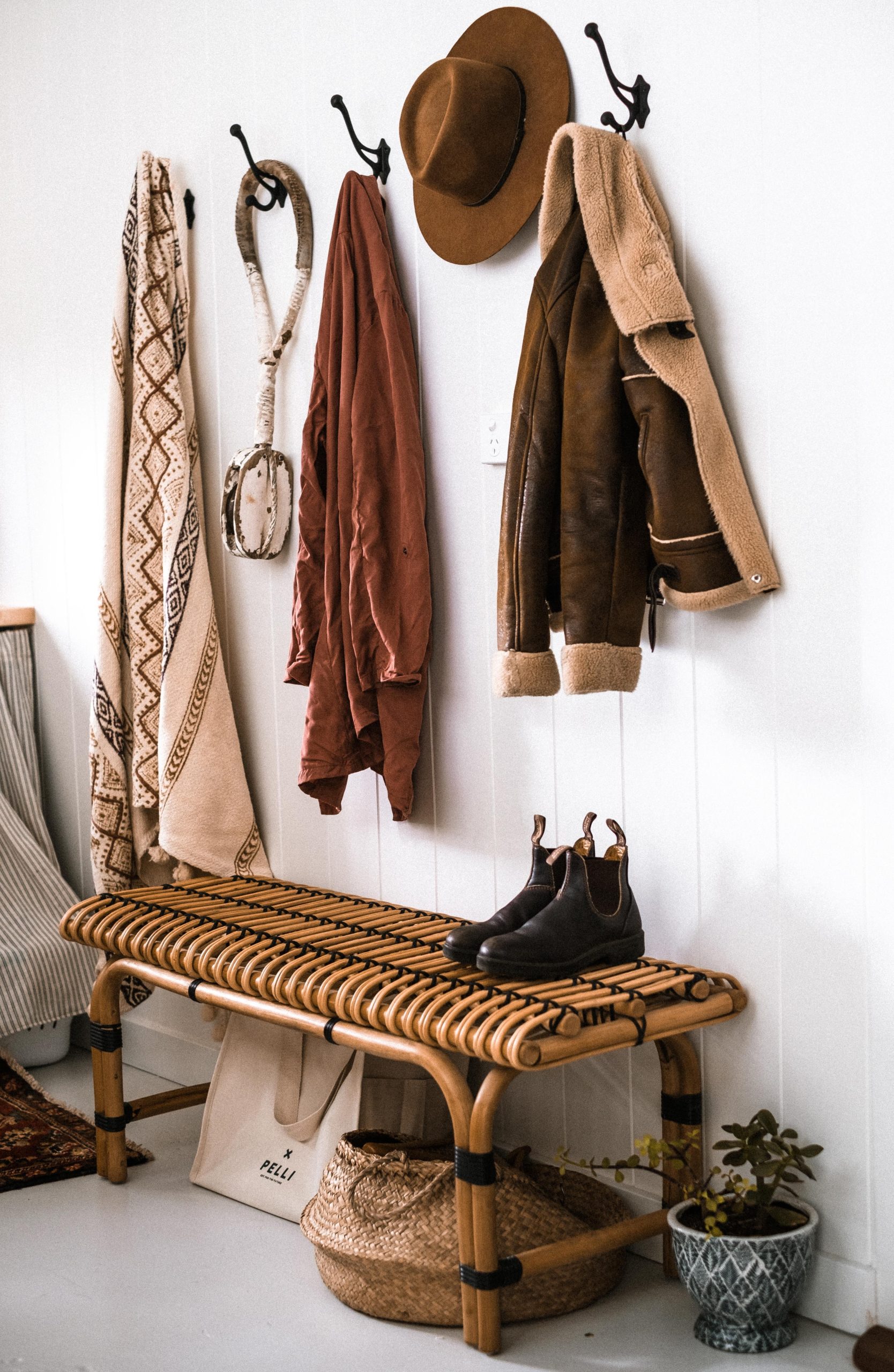Warm rustic entryway showcasing coats, hats, and boots with a woven bench for a homey feel.