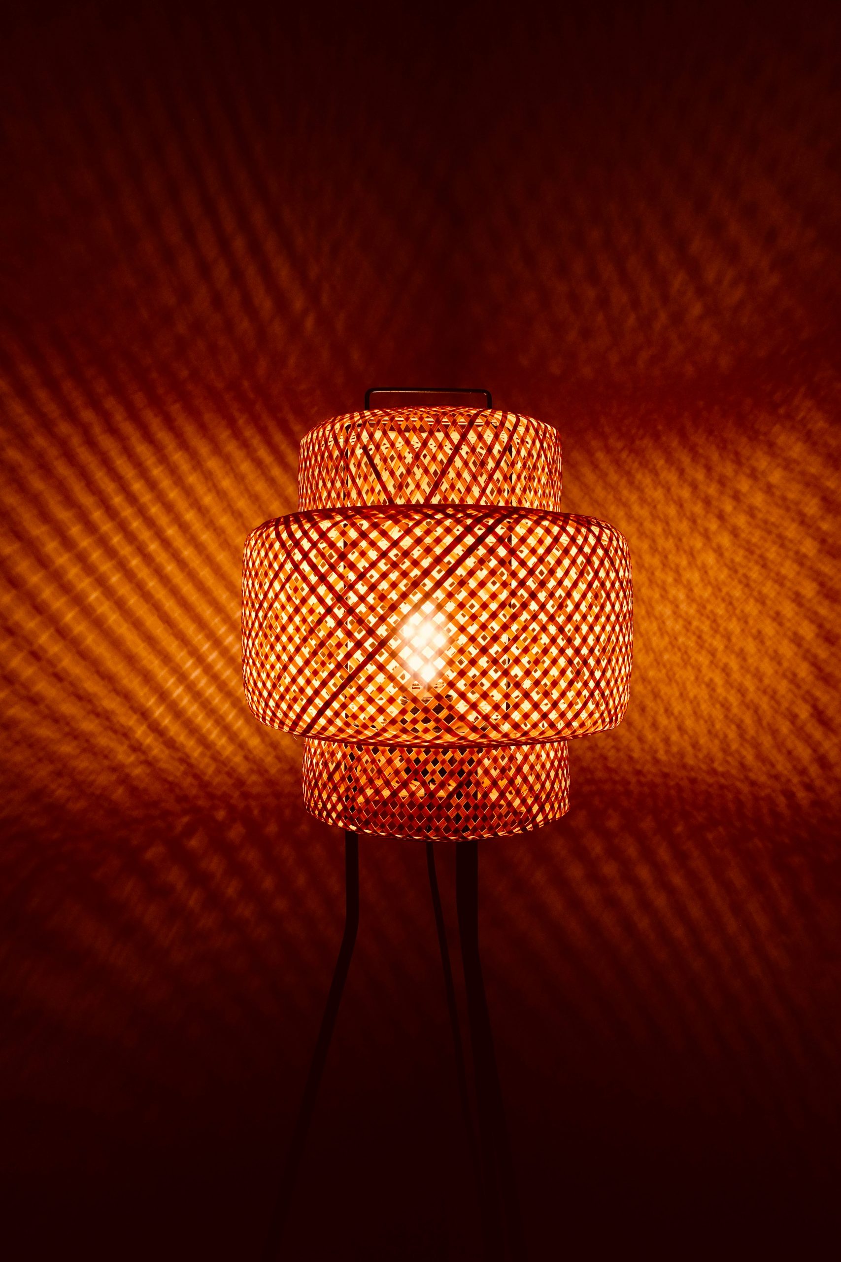 Woven bamboo lamp casting patterned light on wall