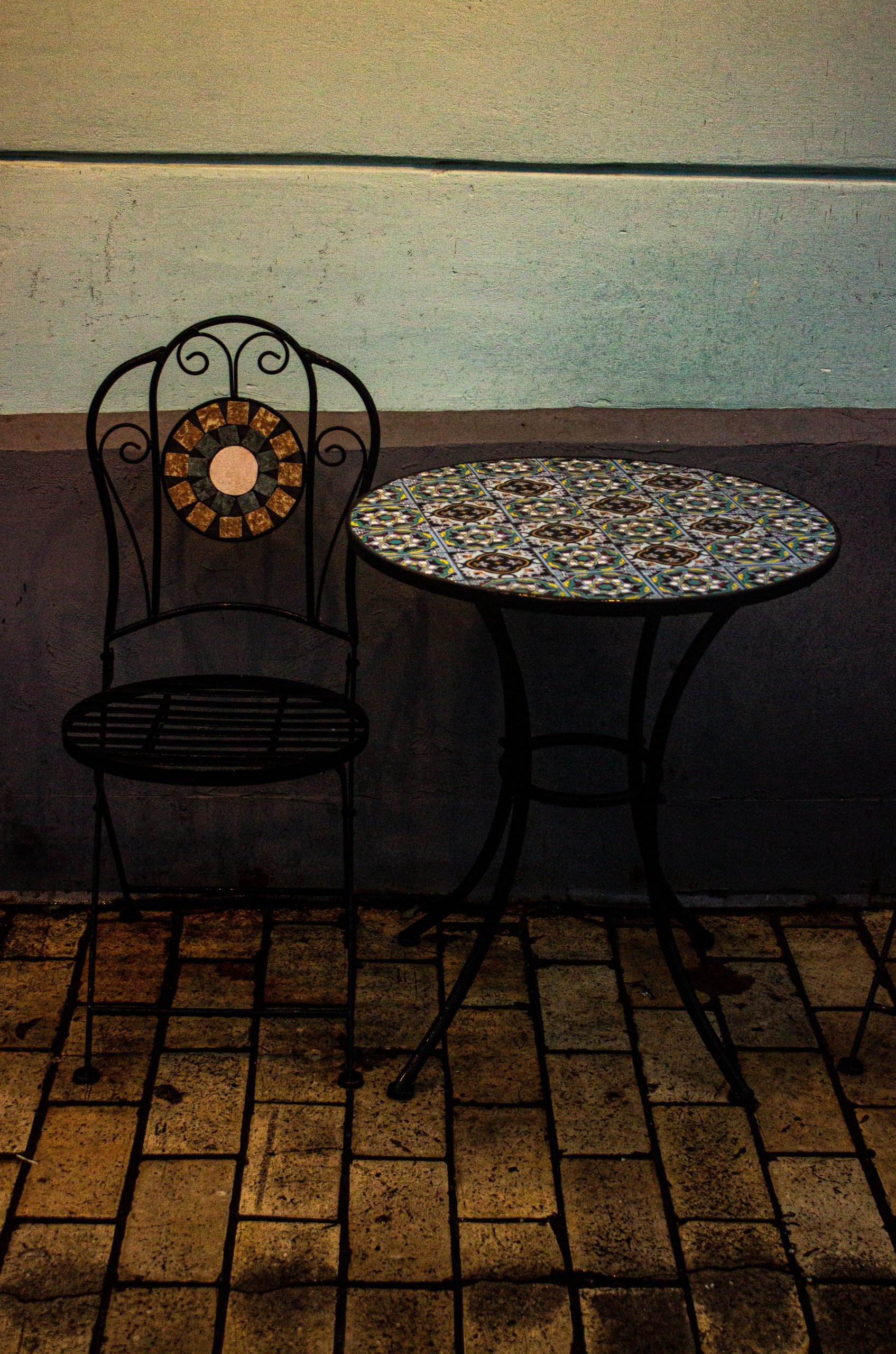 Wrought iron chair and mosaic table on tiled pavement, perfect for patios.