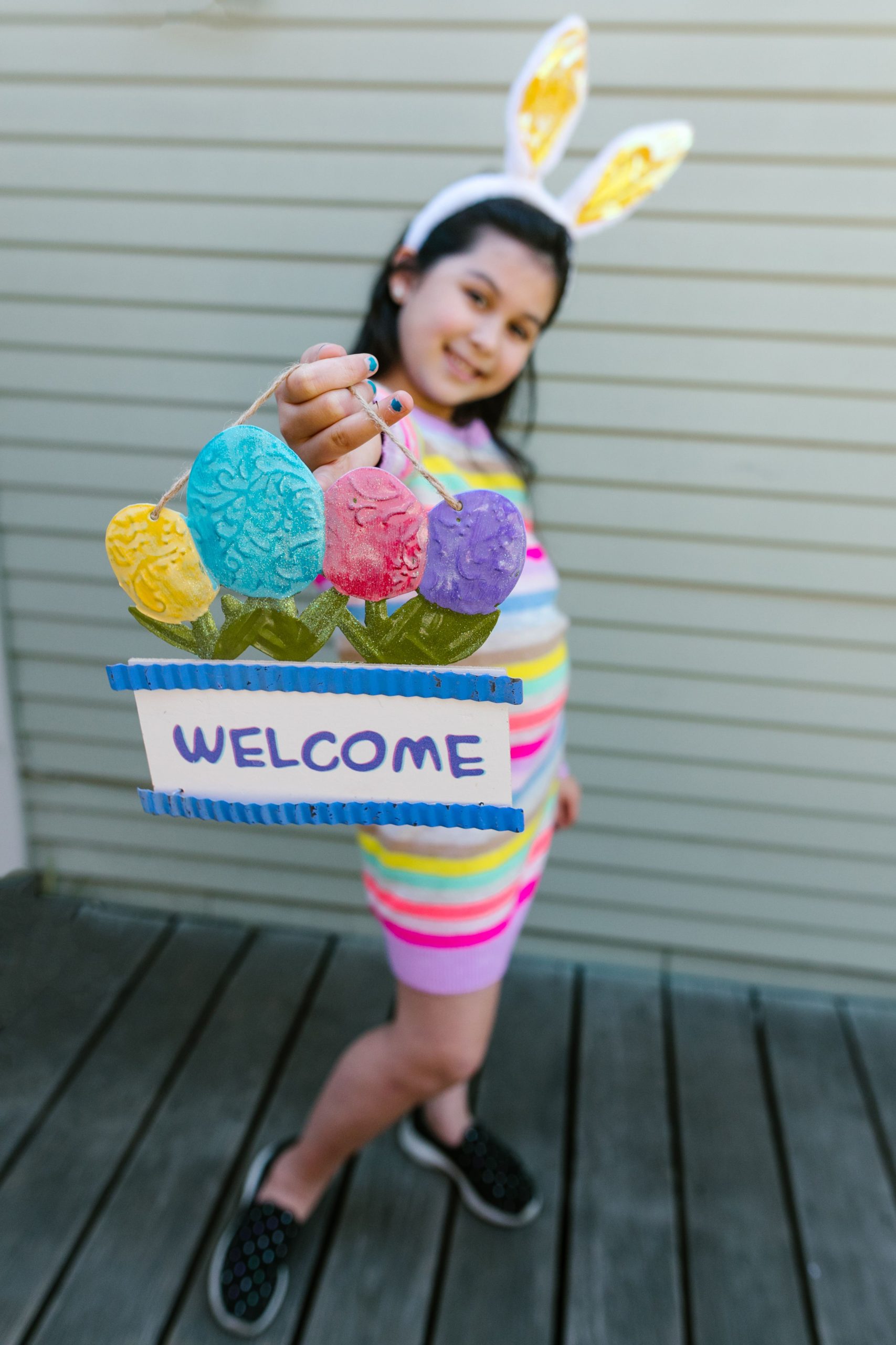 Young girl holding a colorful Easter-themed welcome sign outdoors, celebrating spring.