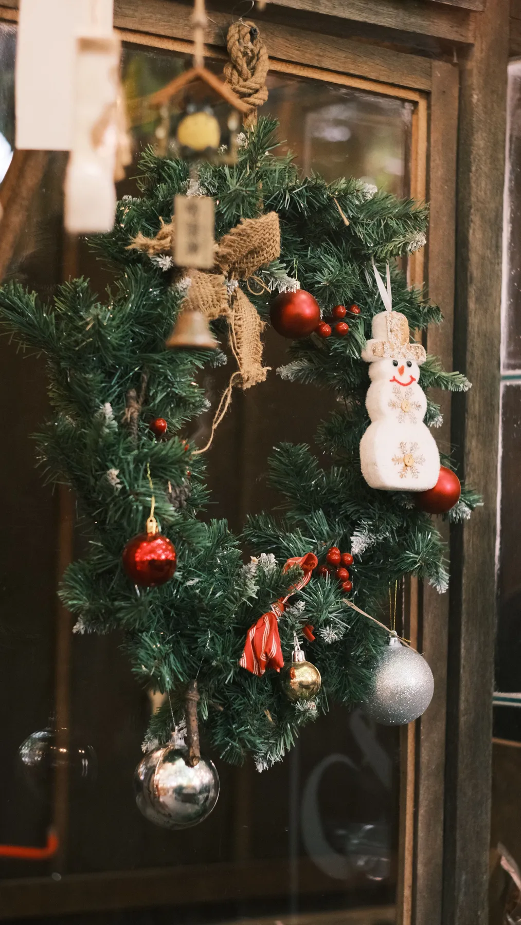 A beautiful Christmas wreath with a snowman, red ornaments, and green foliage on a rustic door.