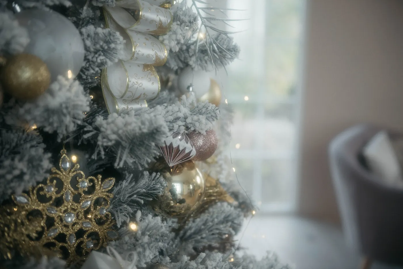 A beautifully decorated Christmas tree with gold and white ornaments, ribbon, and lights indoors.