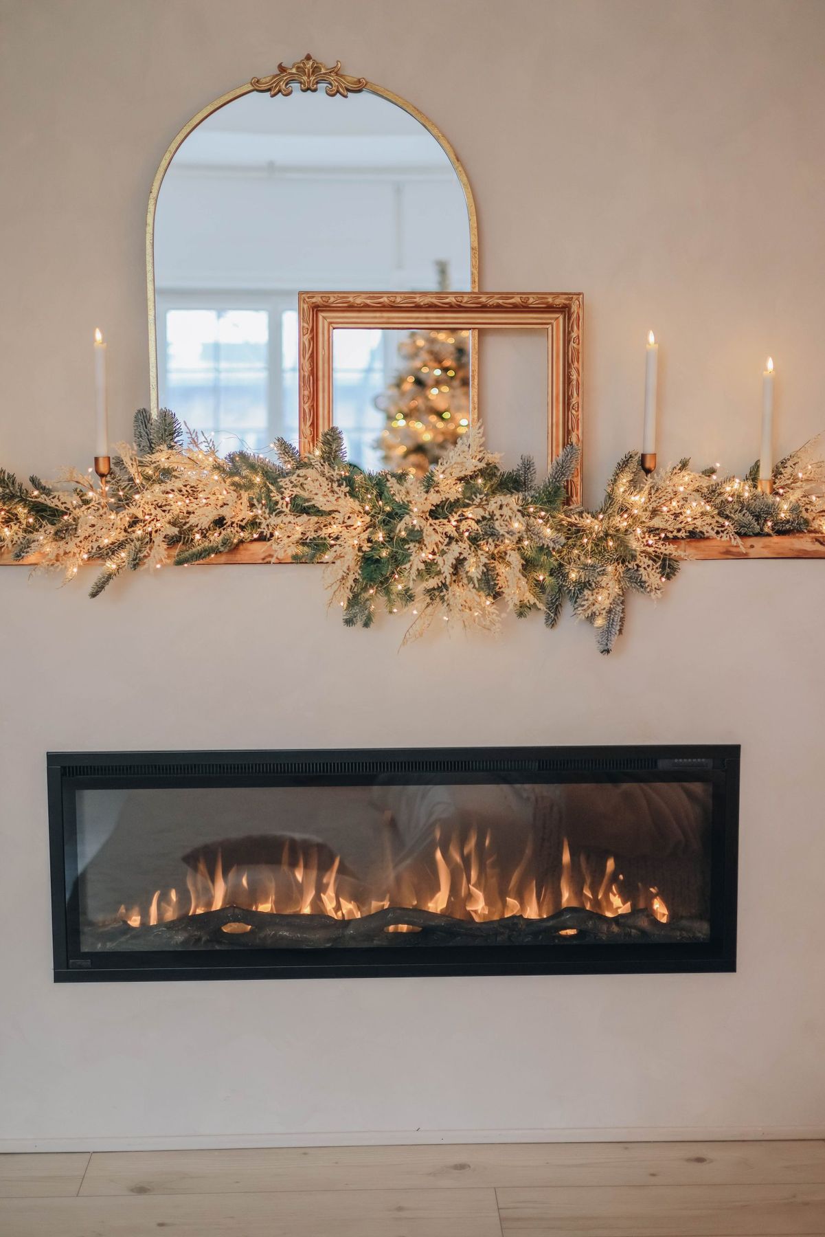A beautifully decorated fireplace for Christmas with candles, greenery, and a festive reflection in mirrors.