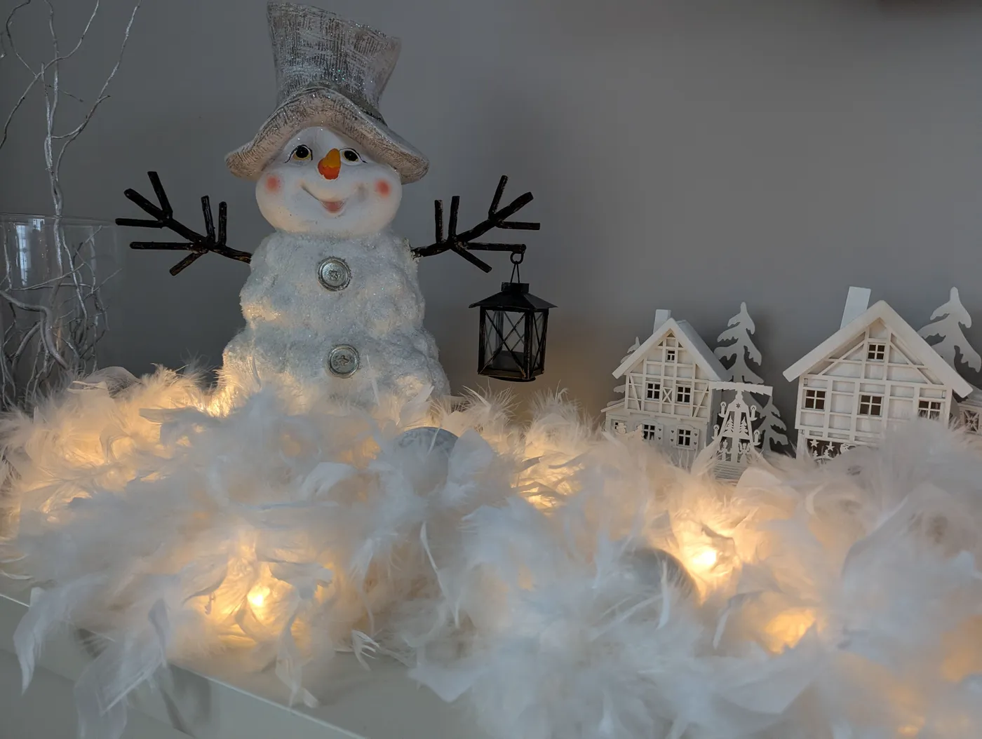 A charming snowman figurine surrounded by soft feathers and warm glowing lights for Christmas decor.