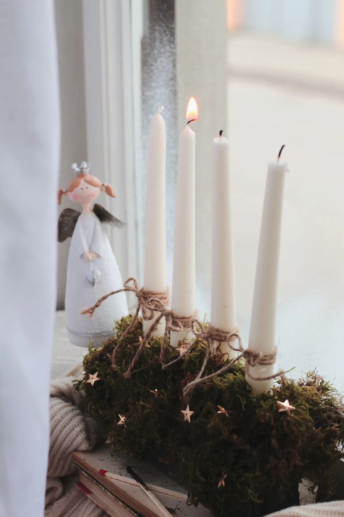 A close-up of glowing Christmas candles and a cute angel figurine adorning a windowsill.