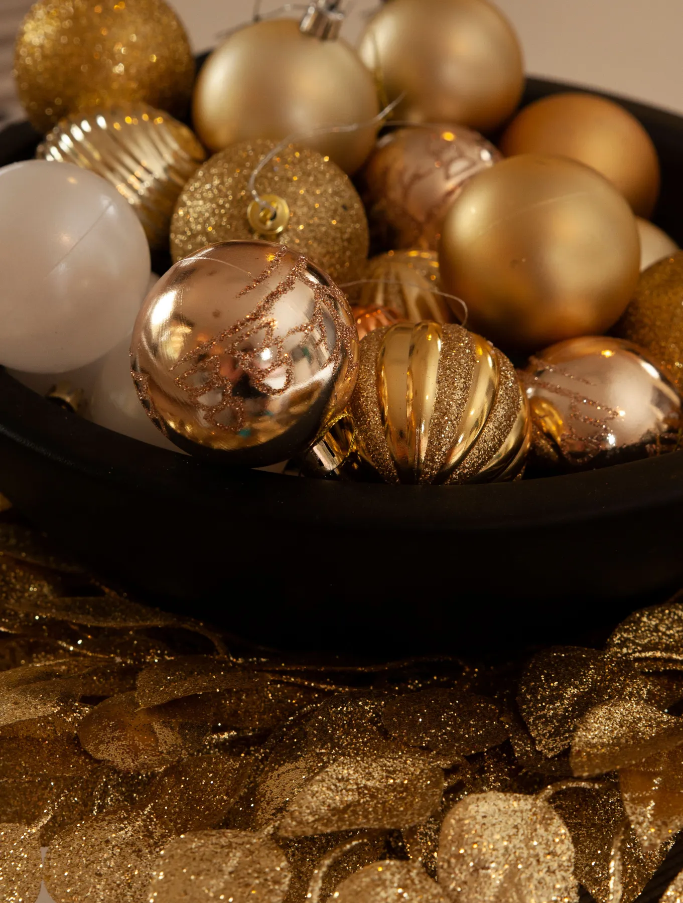 A close-up of gold and silver Christmas ornaments in a black bowl, creating a festive and luxurious holiday atmosphere.