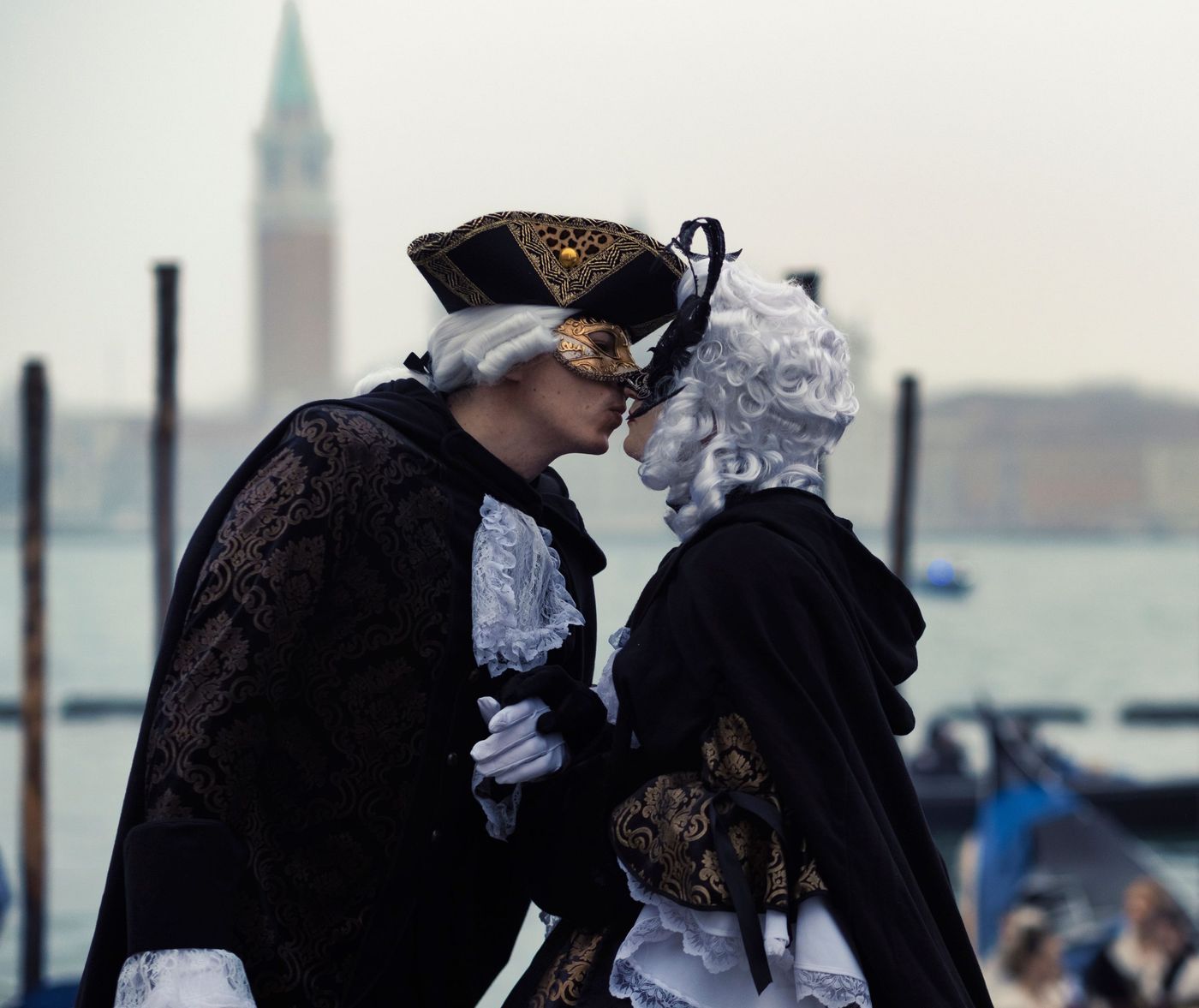 A couple in elaborate costumes and masks share a tender moment in Venice.