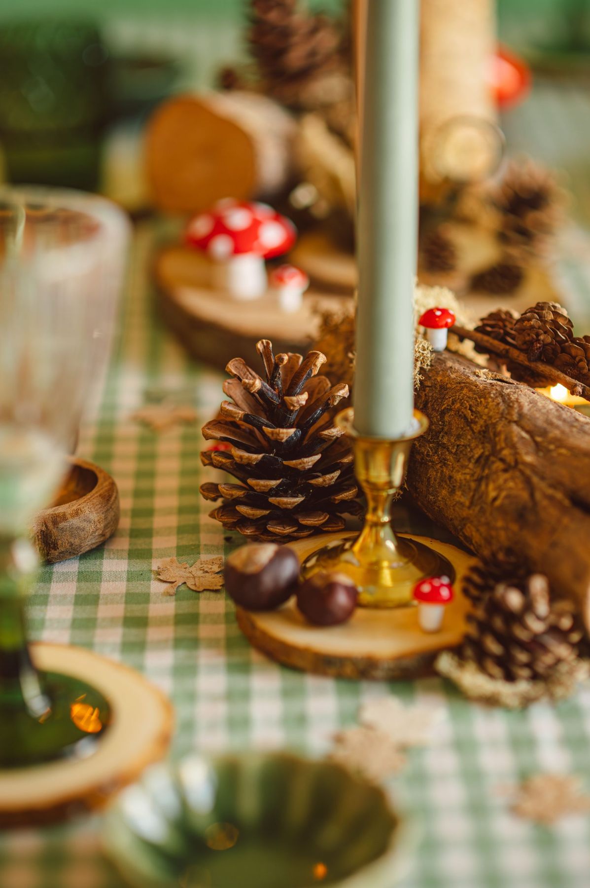 A cozy fall table setting with pinecones, mushrooms, and a candle on a checkered cloth.