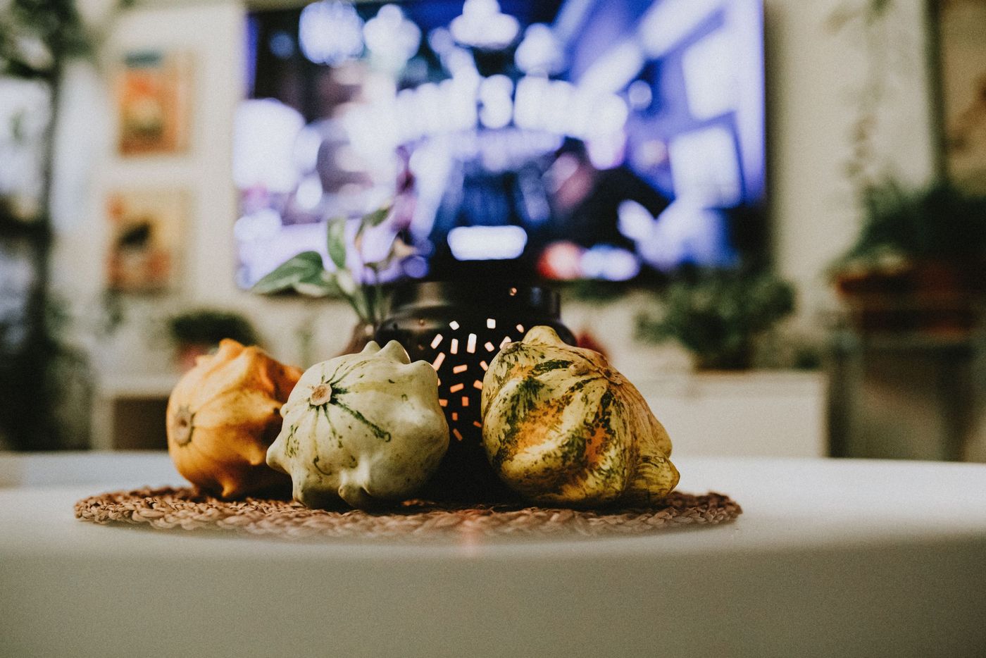 A cozy indoor setting featuring decorative gourds on a woven mat with a blurred television background.