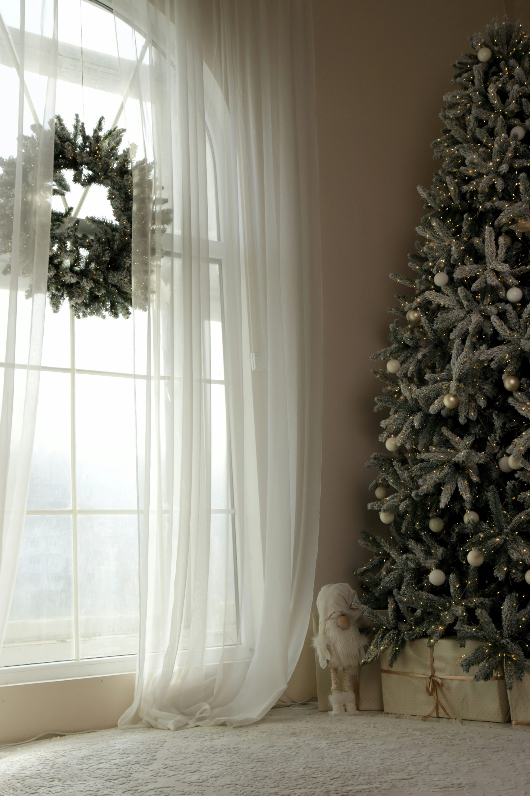A decorated christmas tree and wreath by a window