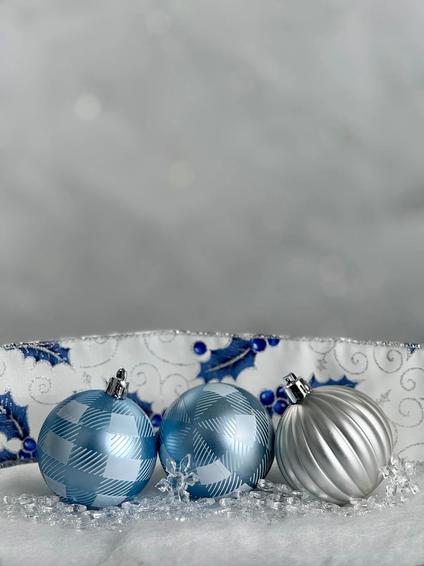 A festive arrangement of blue and silver Christmas baubles on a decorative fabric.