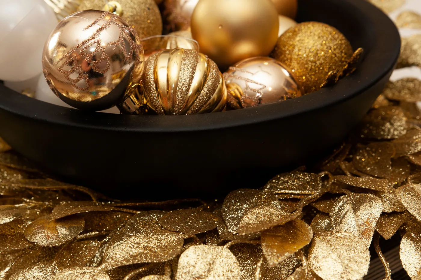 A festive display of gold and bronze Christmas ornaments in a black bowl, perfect for holiday decoration themes.