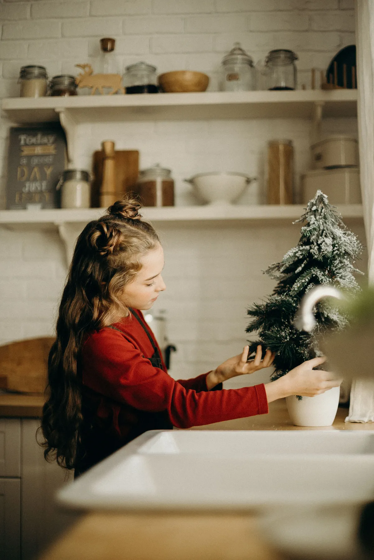 A girl decorating a small Christmas tree on a kitchen counter with cozy interior accents.