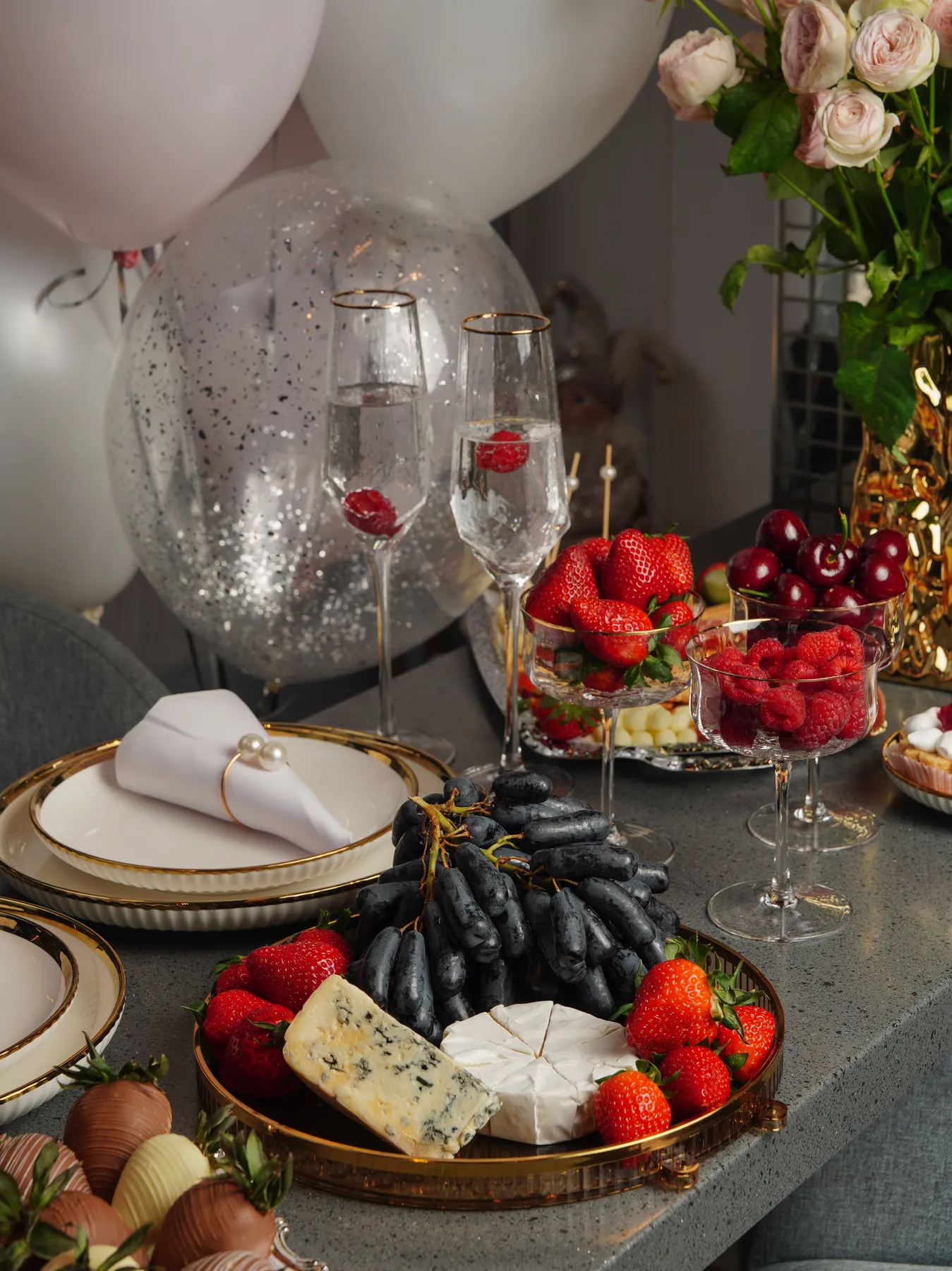 A luxurious table setting with assorted fruits, cheese, champagne, and balloons for a festive occasion.