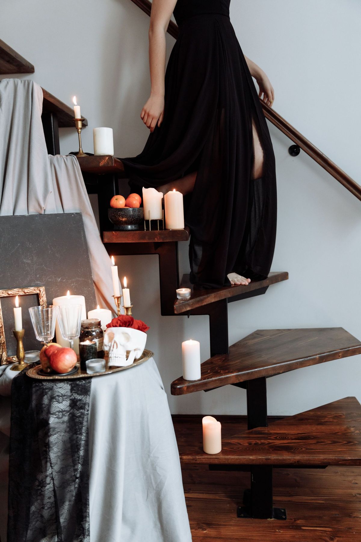 A person descends wooden stairs adorned with candles and elegant decor, wearing a flowing black dress.