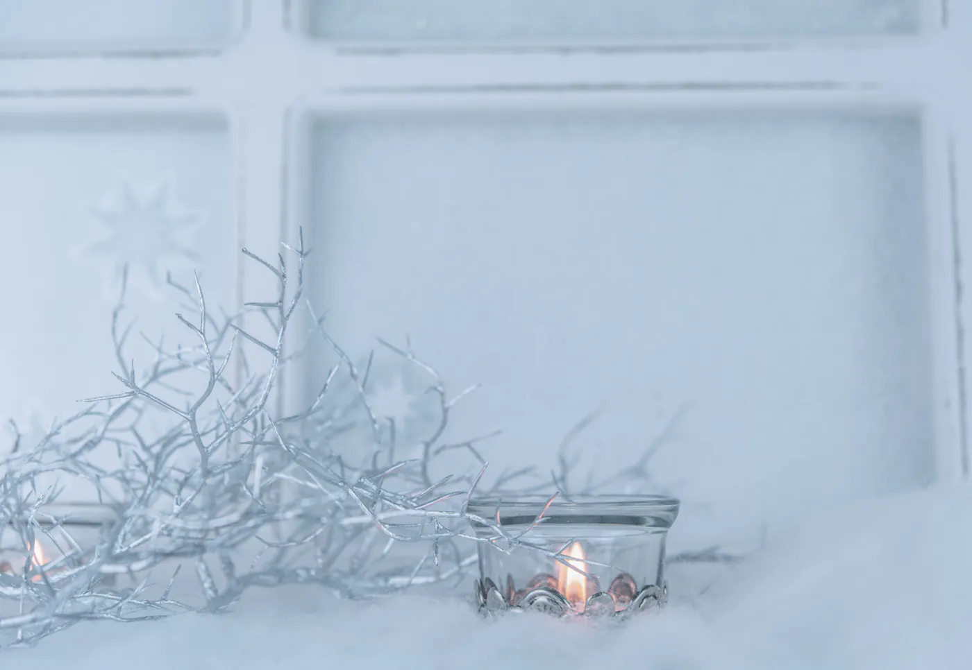 A serene winter scene with lit candles and delicate silver twigs against a frosted background, capturing the coziness of the season.