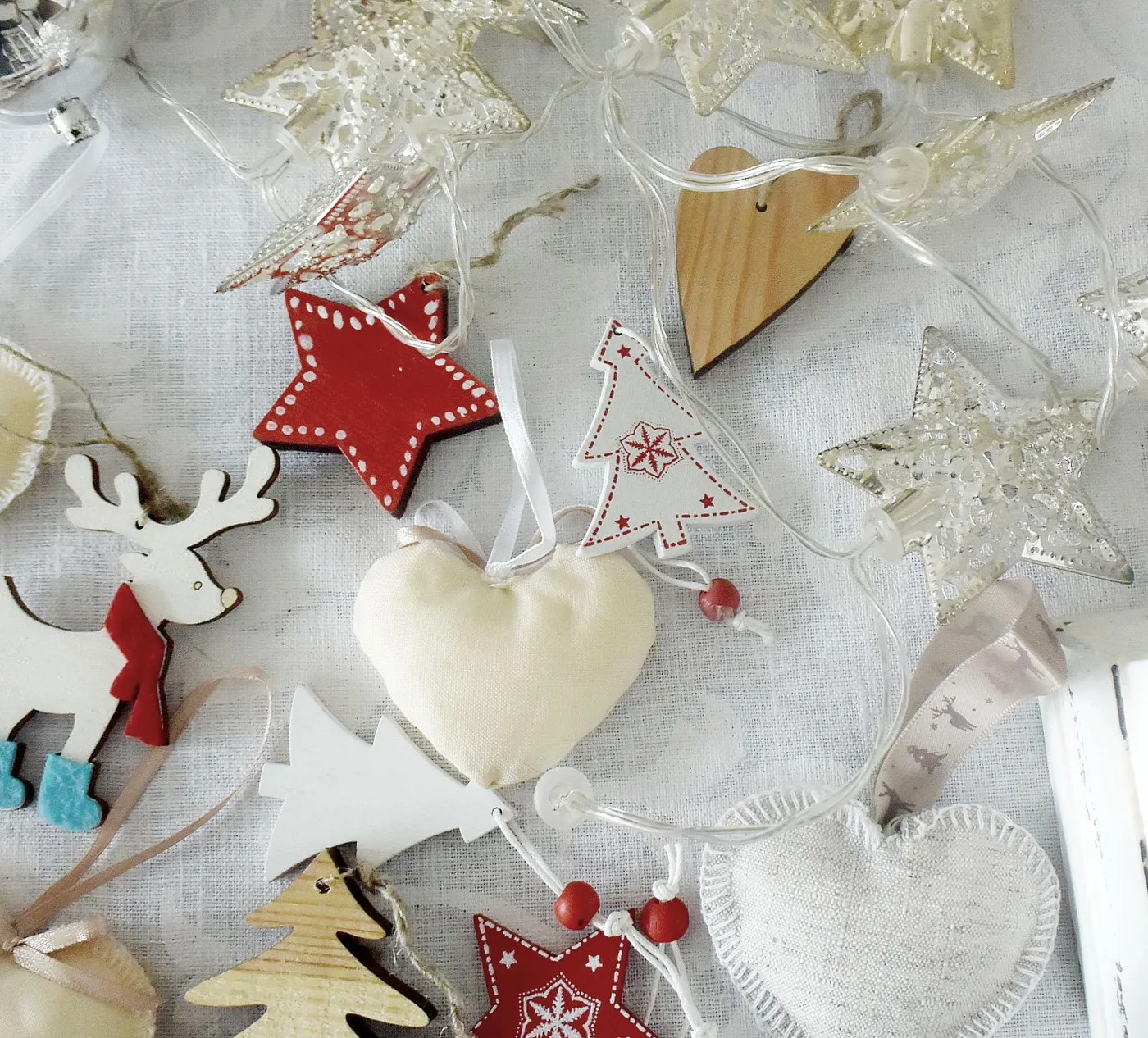 A variety of Christmas decorations including stars, reindeer, and hearts on a white tablecloth.