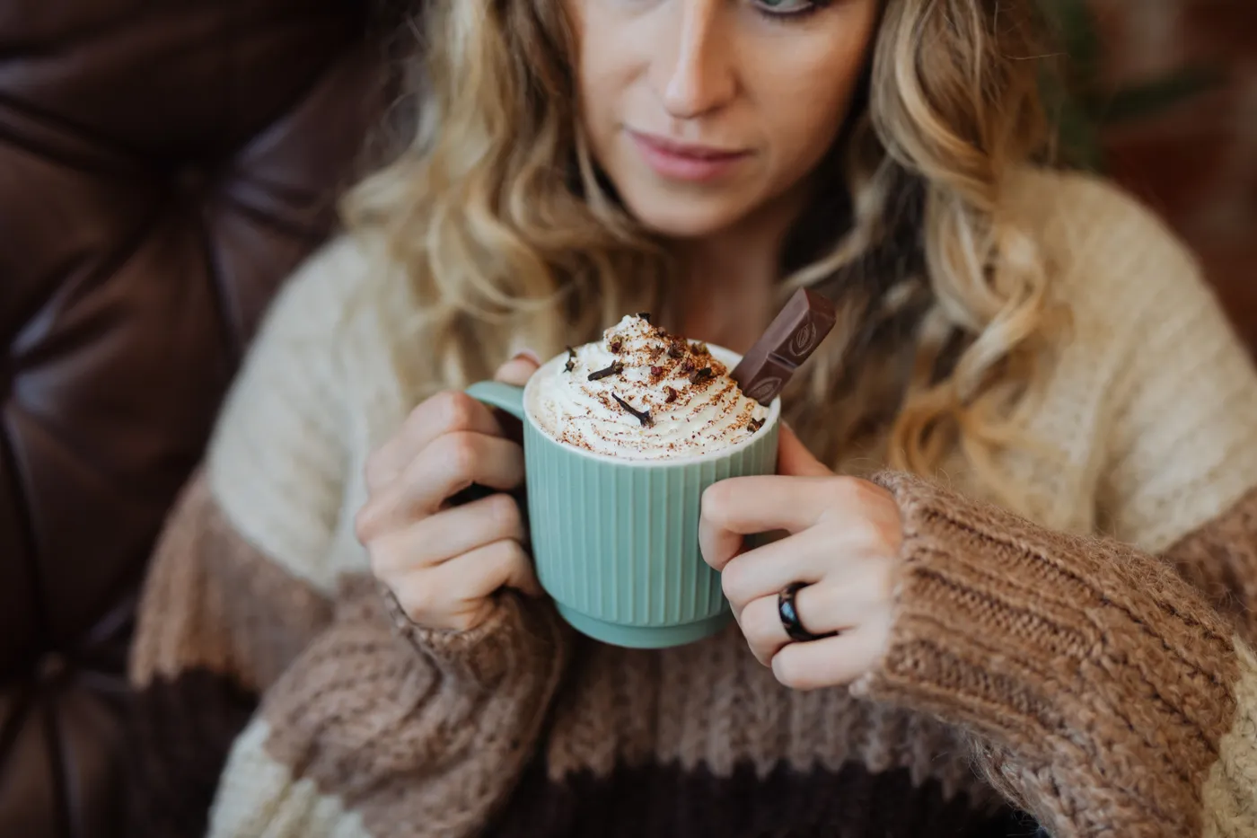 A woman enjoys hot cocoa with whipped cream in a cozy setting, perfect for autumn.