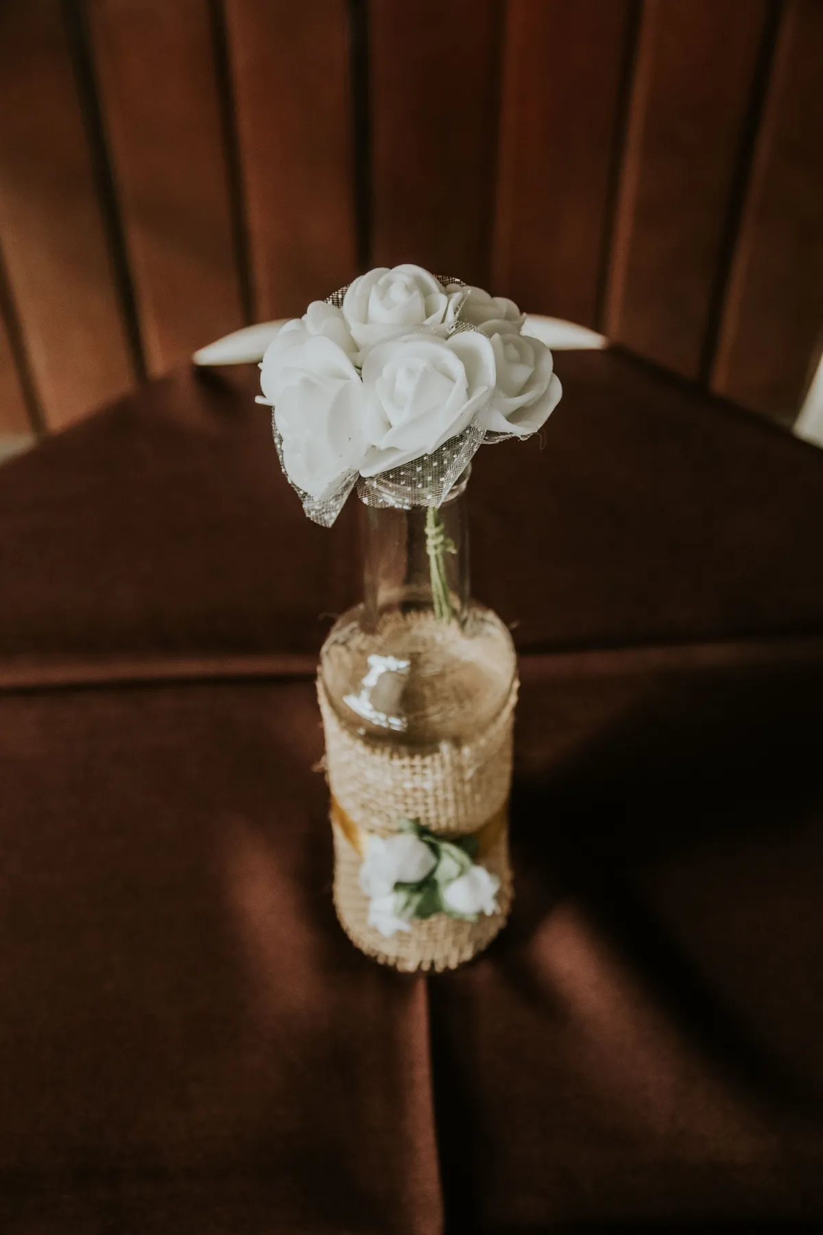 Aesthetic still life of white flowers in a burlap-wrapped glass bottle on a dark background.