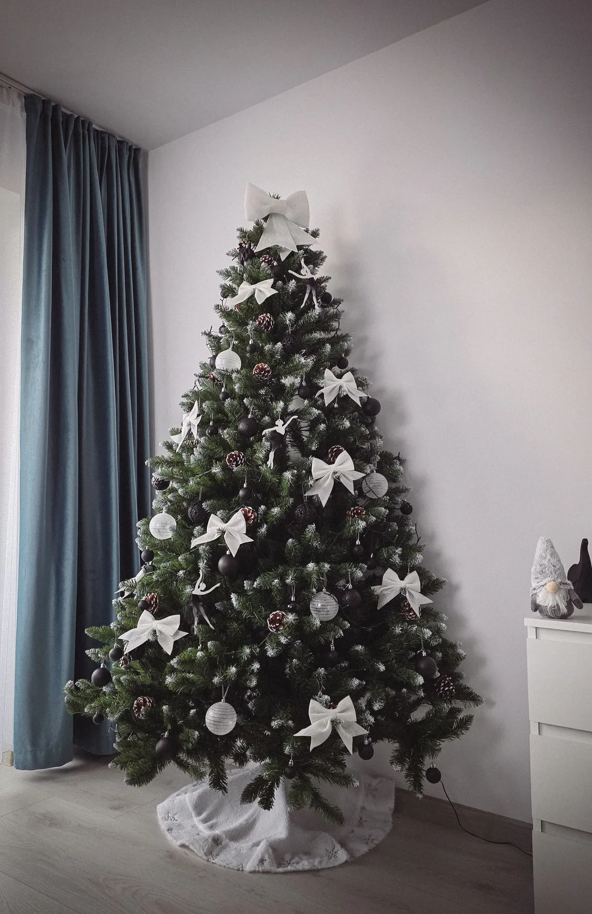 Beautifully decorated Christmas tree with white bows and silver ornaments in a cozy indoor setting.