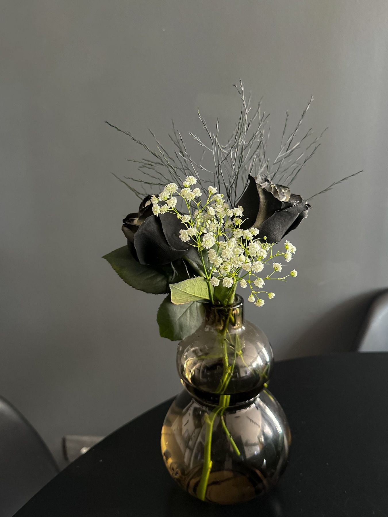 Black roses and delicate flowers in a vase on a dark table, perfect for modern decor themes.