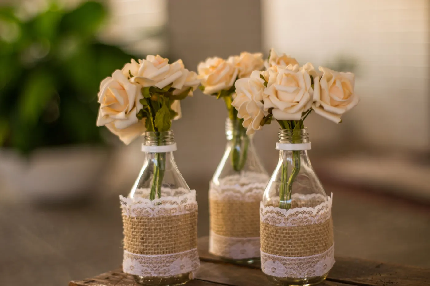 Charming display of cream roses in handcrafted lace-covered vases on a rustic table.
