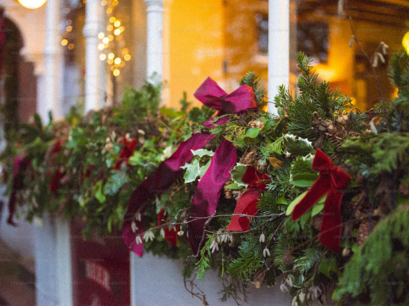 Christmas garland with red bows on a porch railing - Photo on Unsplash+