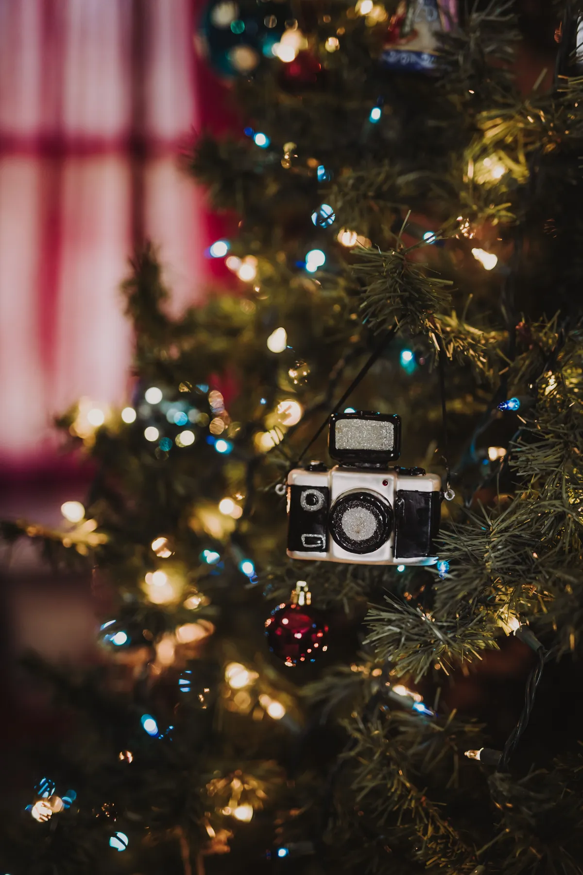 Close-up of a classic camera ornament hanging on a Christmas tree with lights.