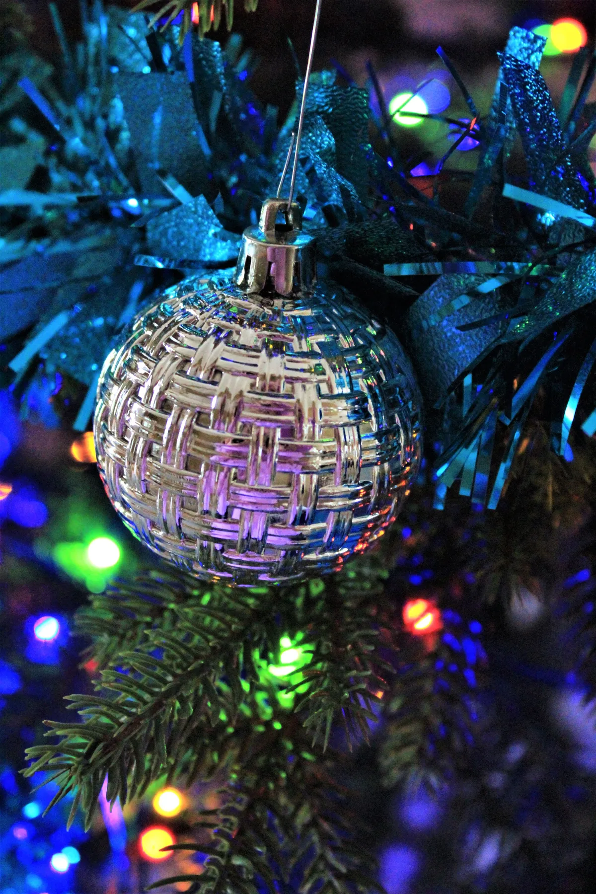 Close-up of a silver ornament on a Christmas tree adorned with colorful lights, evoking holiday spirit.