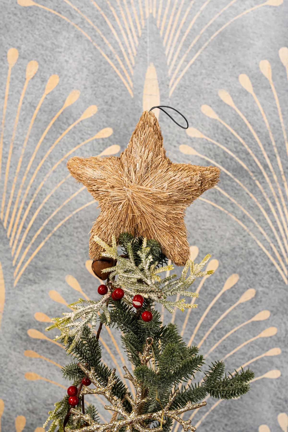 Close-up of a straw star ornament atop a Christmas tree branch indoors.