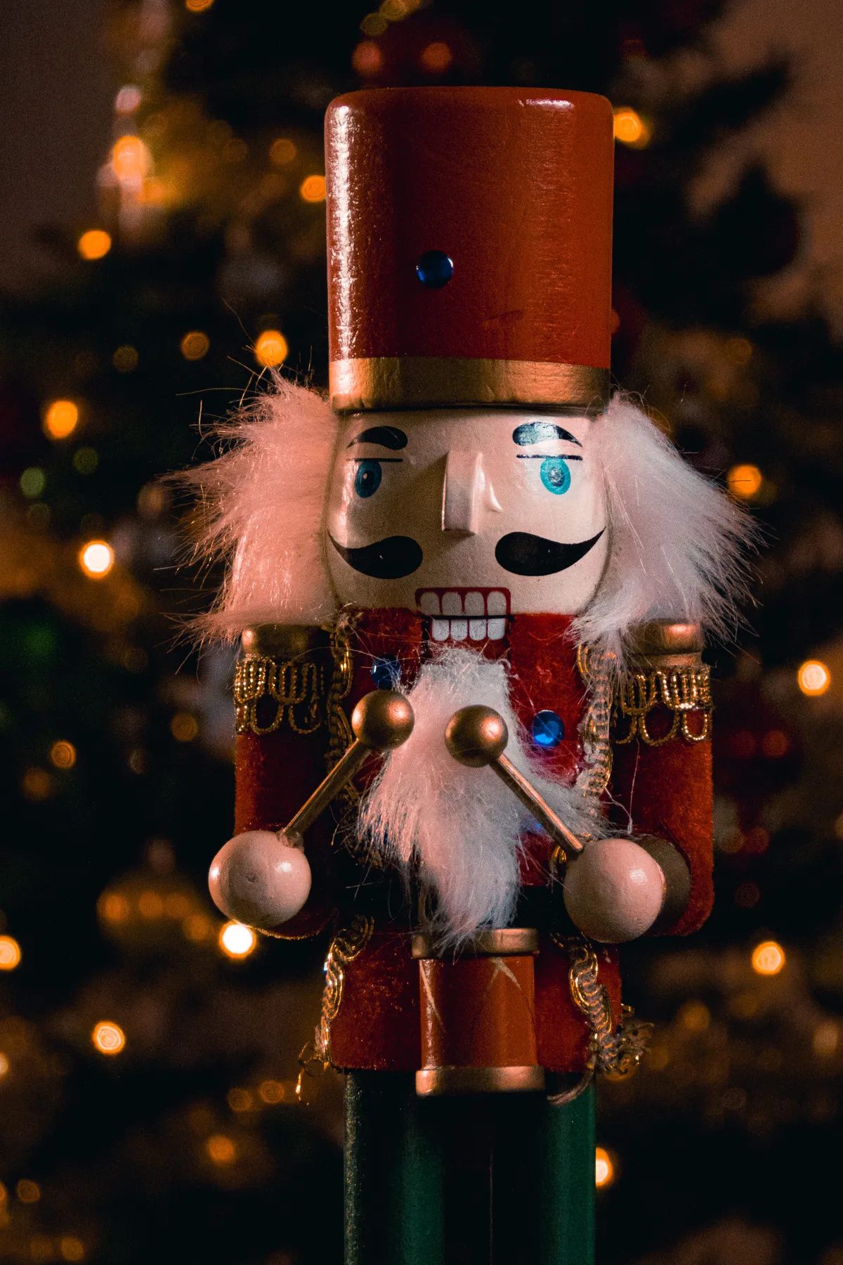 Close-up of a traditional nutcracker against a glowing, decorated Christmas tree.