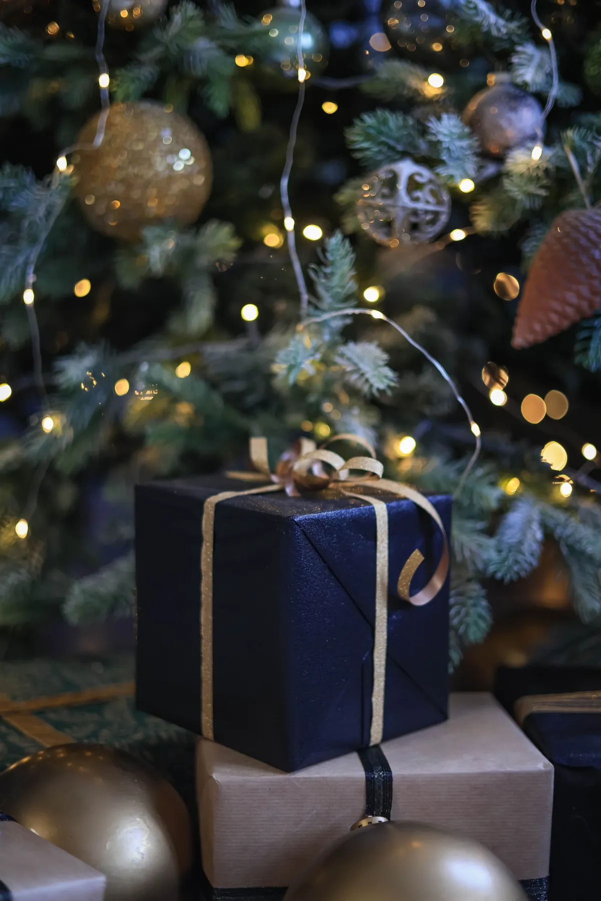 Close-up of Christmas gifts under a decorated tree with lights.