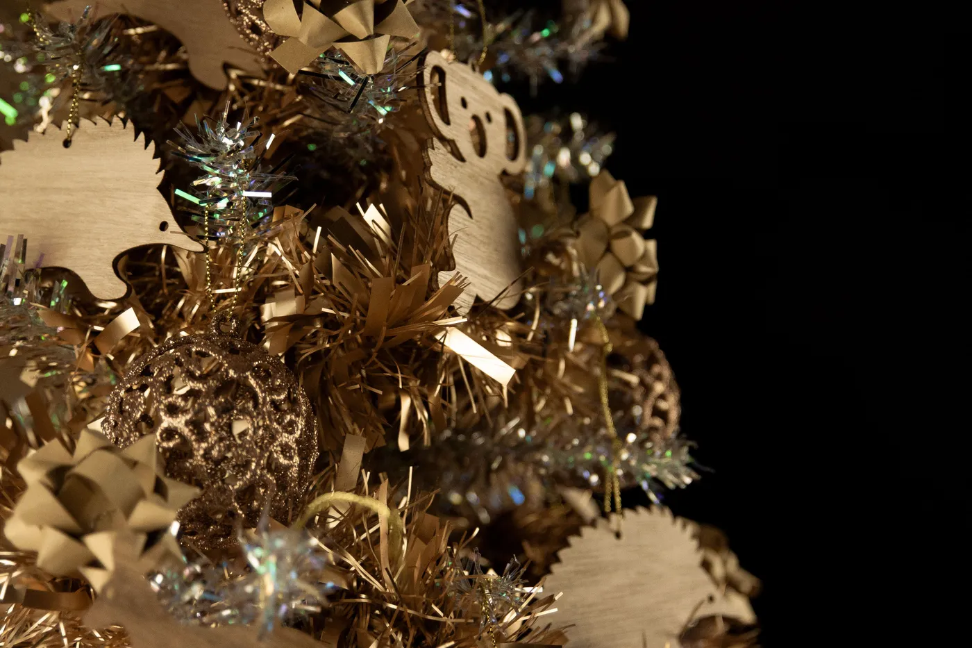 Close-up of gold Christmas ornaments with tinsel and wooden decorations against a black background.