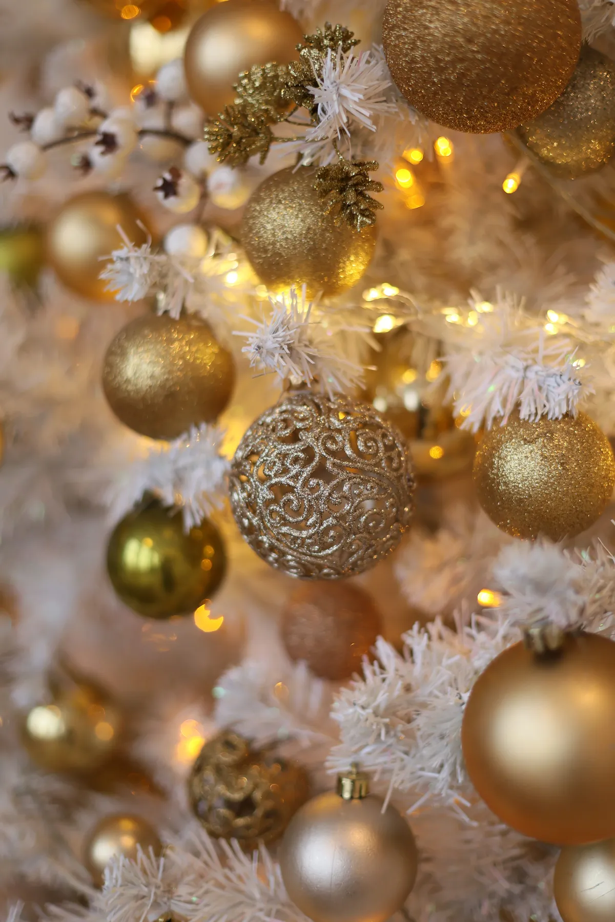Close-up of golden baubles on a white Christmas tree with lights.