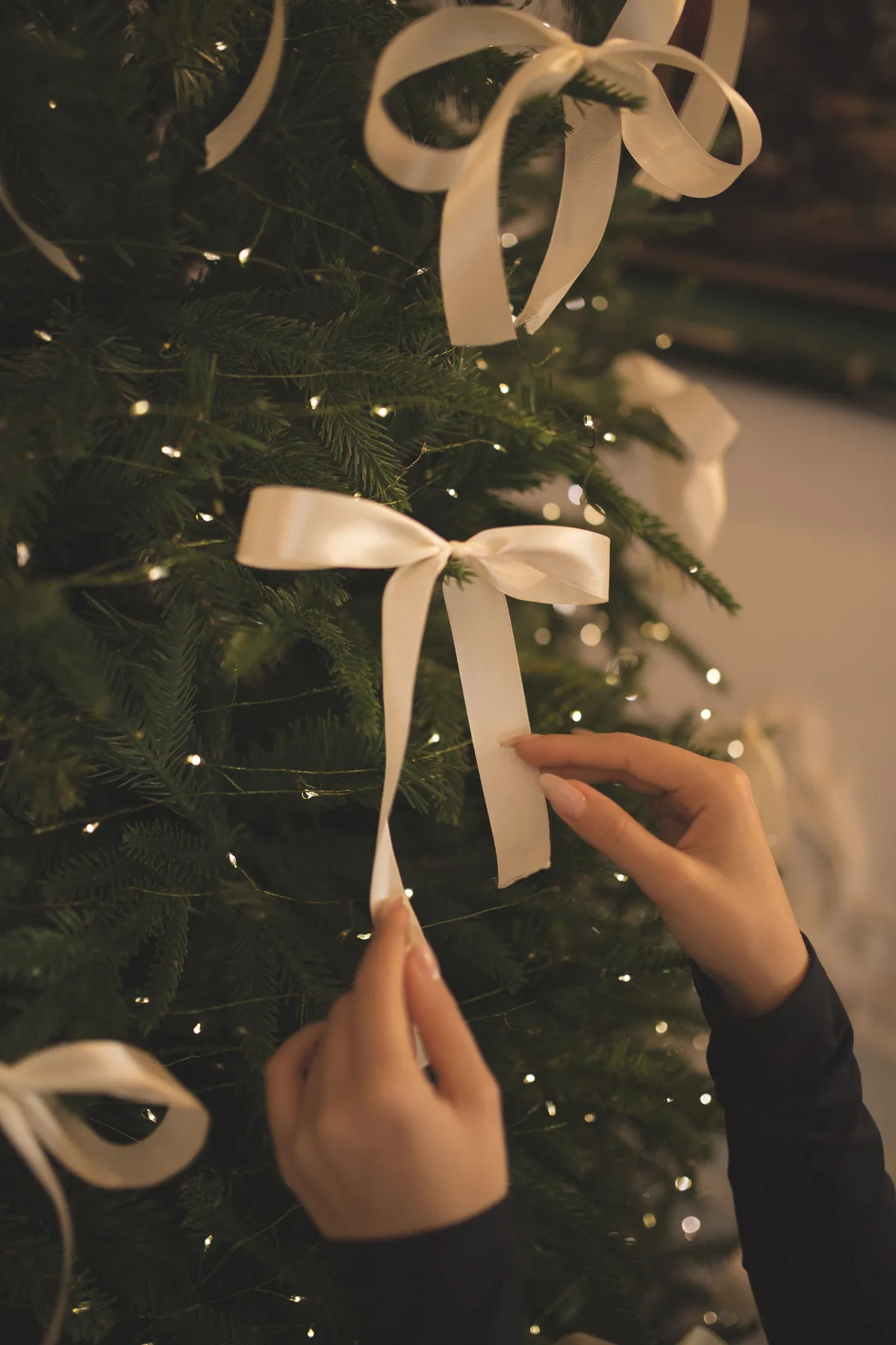 Close-up of hands adding white ribbon to a Christmas tree, creating a festive holiday ambiance.