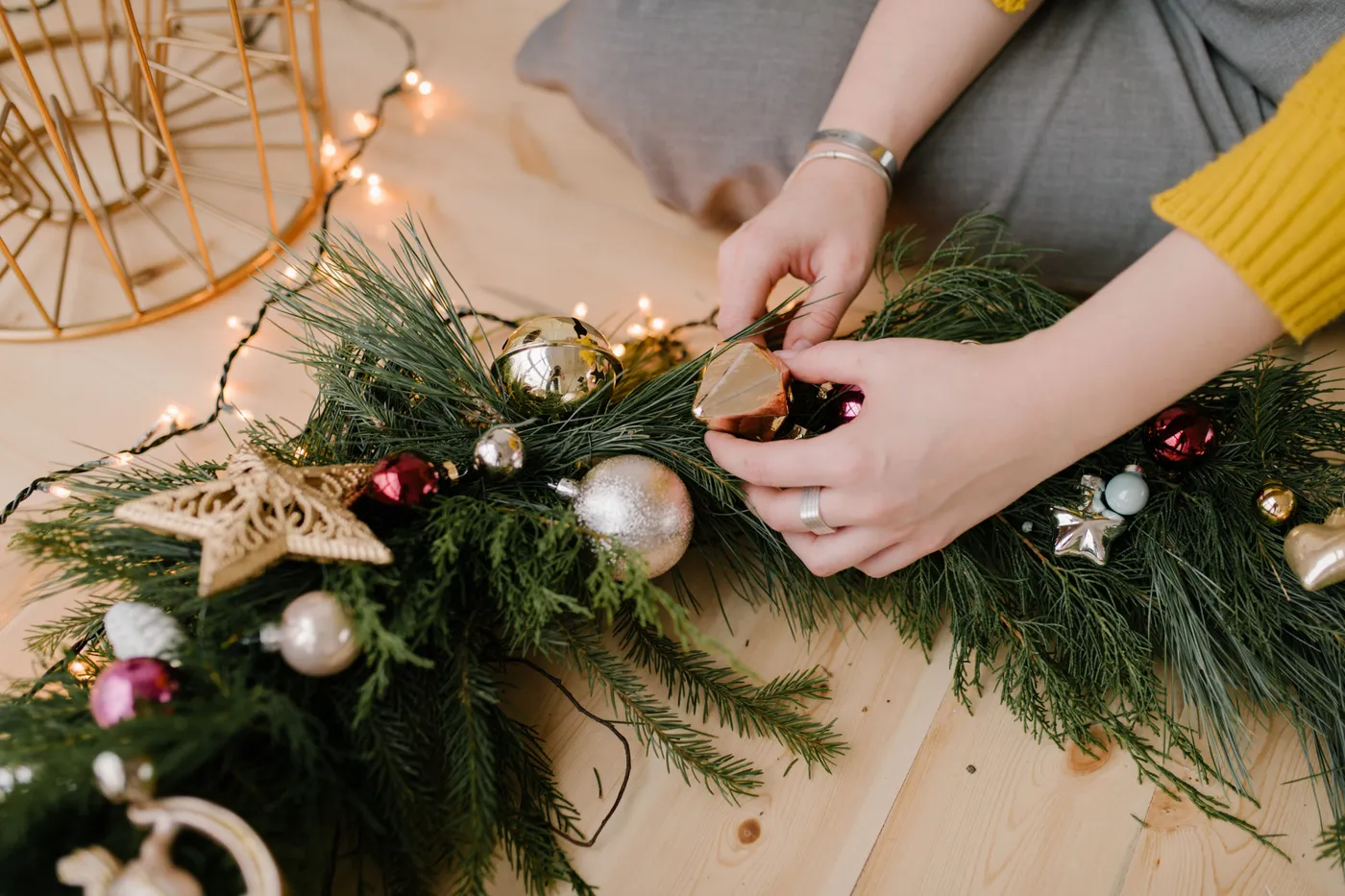 Close-up of hands decorating a Christmas wreath with ornaments, conveying holiday spirit.