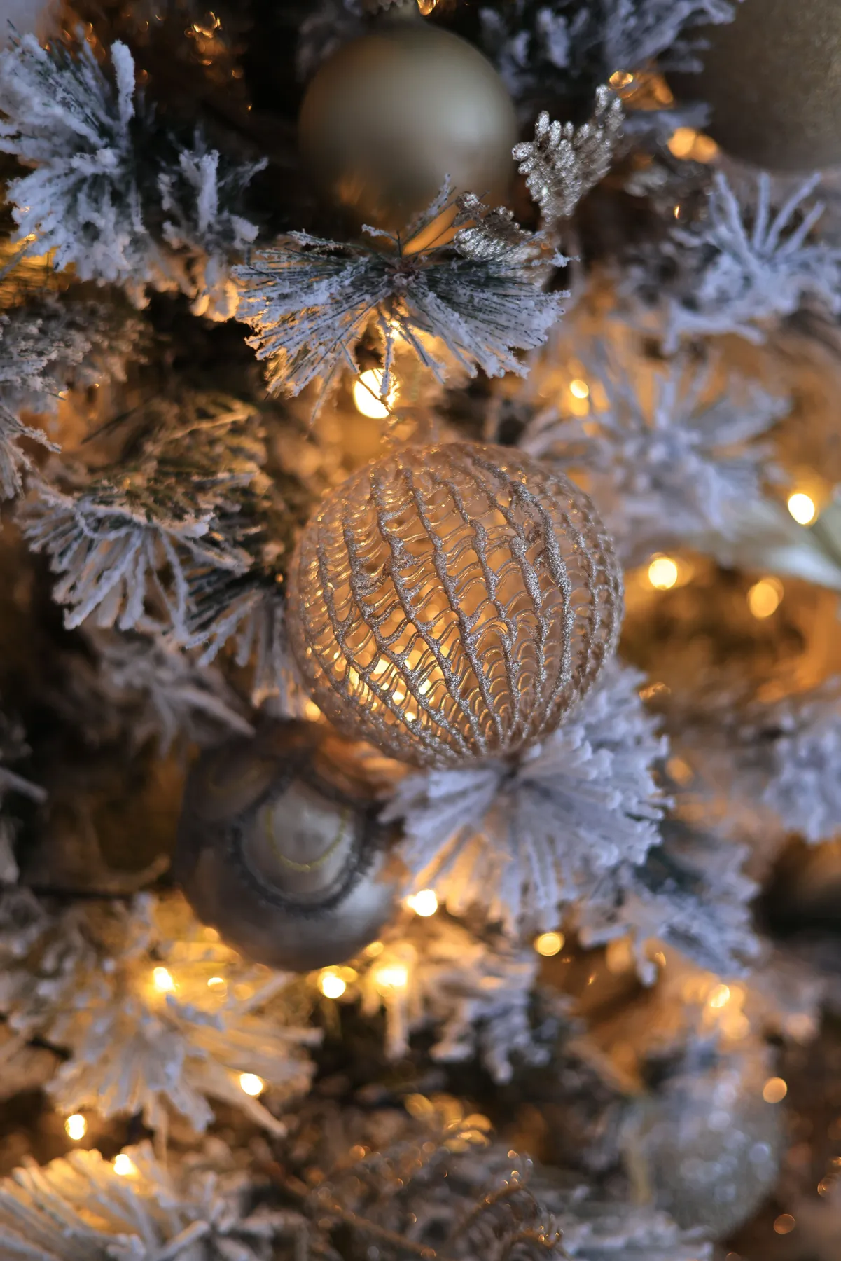 Close-up of illuminated Christmas tree ornaments and frosted branches for a festive ambiance.
