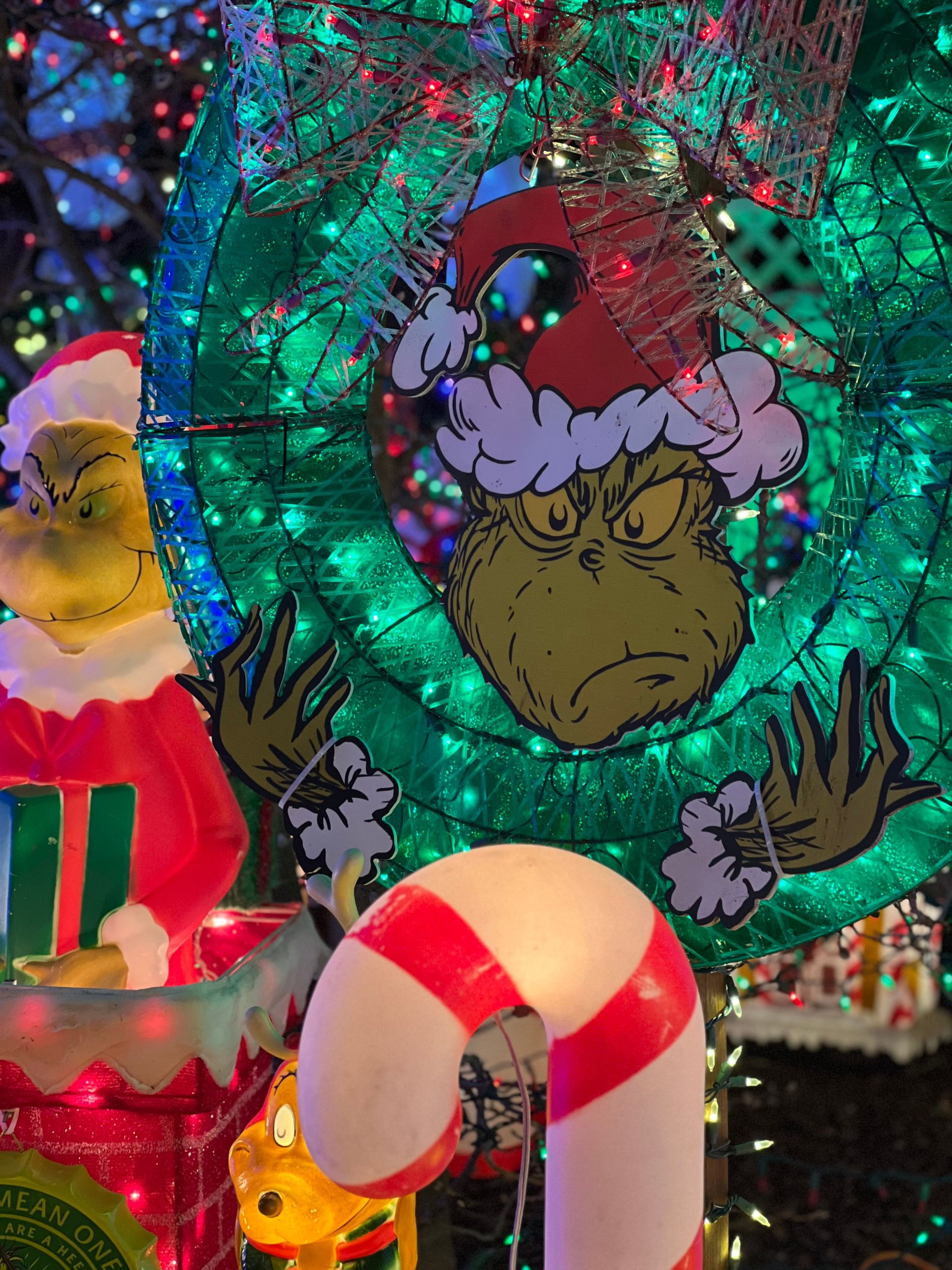 Colorful Christmas scene featuring Grinch decor with lights and candy cane.